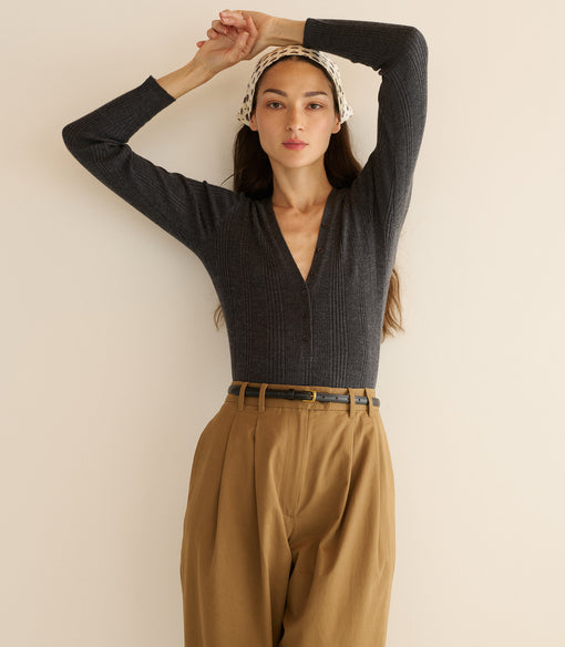 Woman wearing a dark gray long-sleeve top and tan pants against a beige background