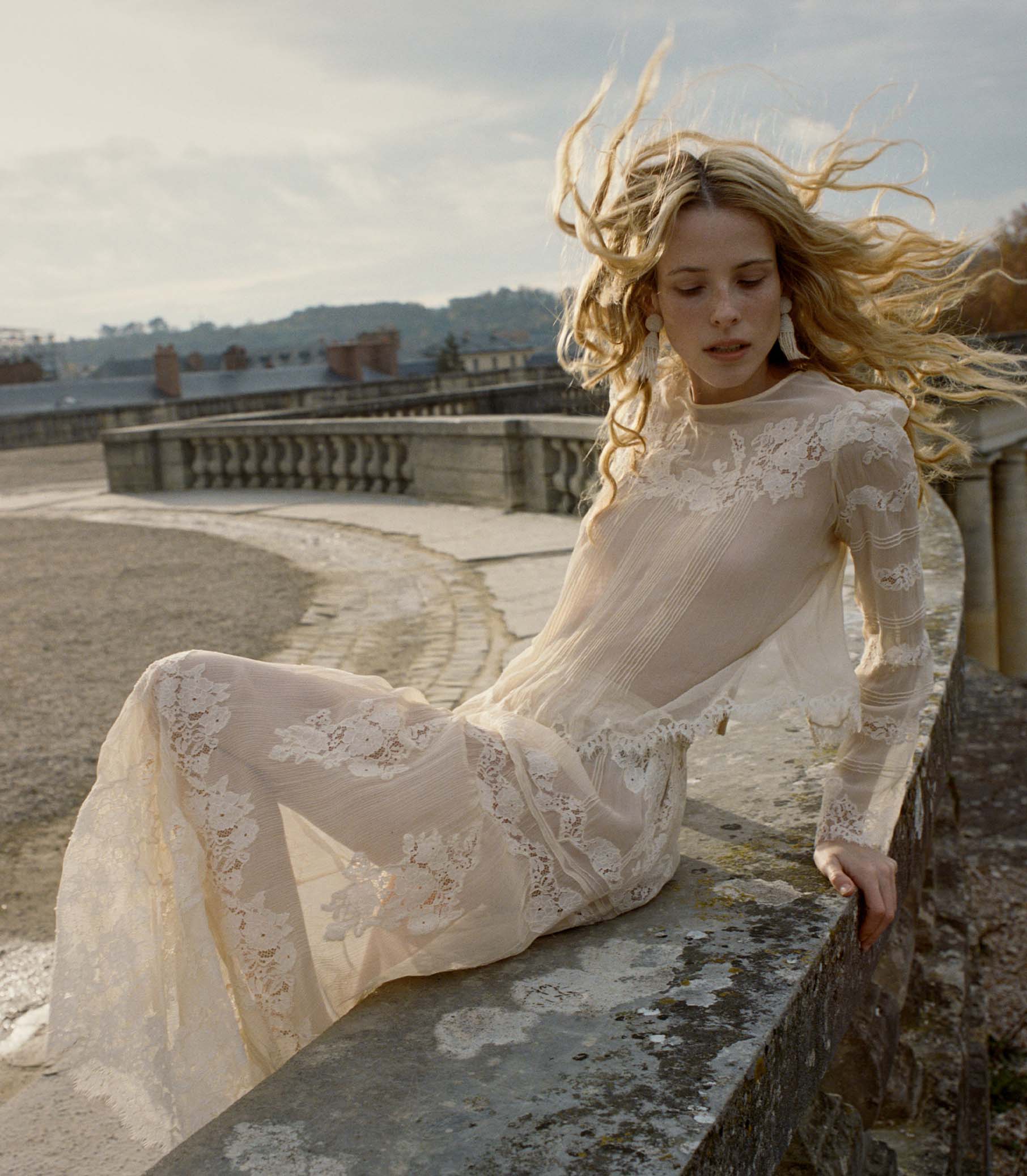 Woman in a lace dress sitting on a stone wall with a scenic background