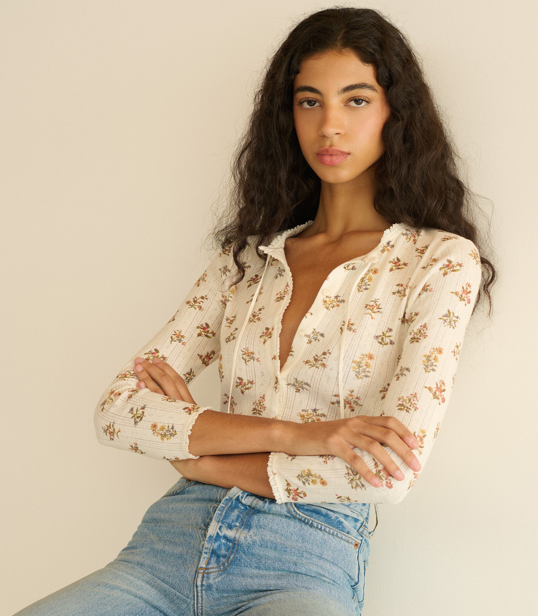 Woman wearing a floral blouse and jeans against a plain background