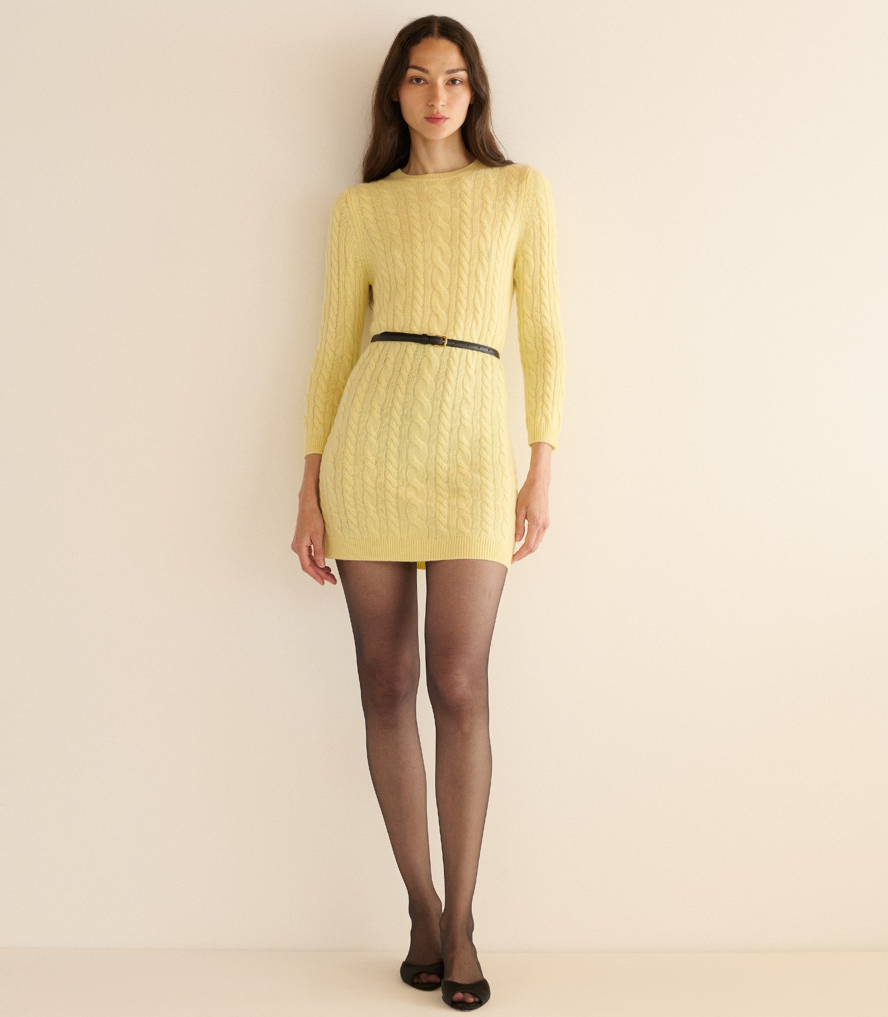 Woman wearing a yellow cable knit dress with a black belt against a beige background 3
