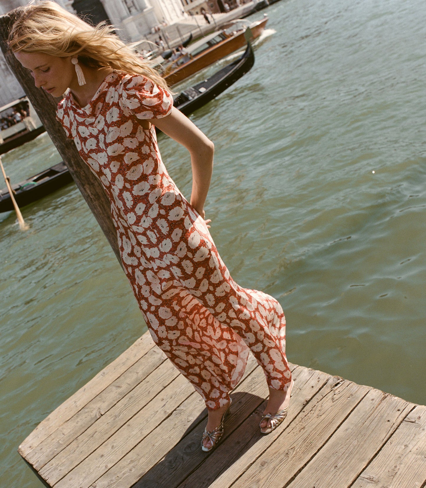Woman in a patterned dress standing on a wooden dock by water