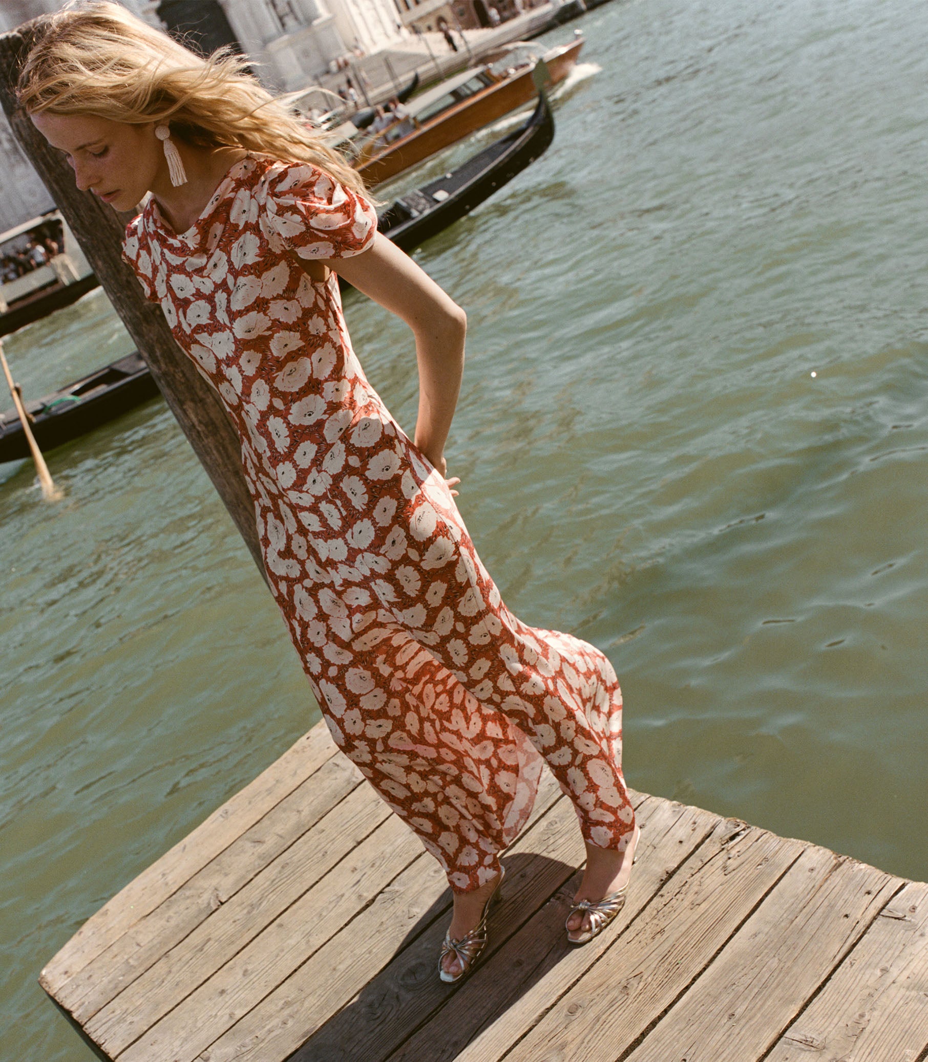 Woman in a patterned dress standing on a wooden dock by water 1