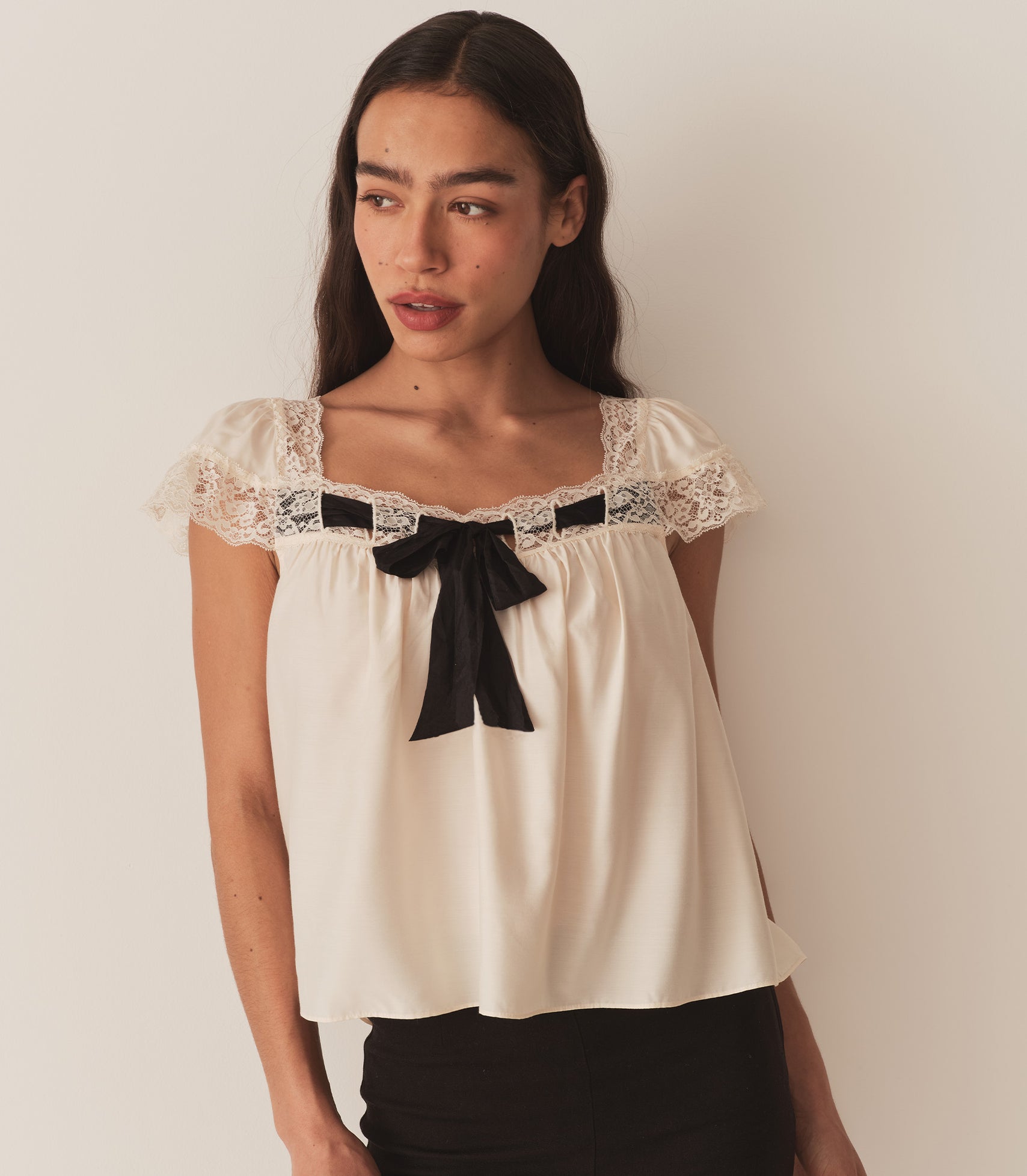 Zahara wears the  Anaya Top, which features a breezy silhouette, delicate flutter sleeves, and a soft V-neckline trimmed with intricate lace and threaded with a contrast silk ribbon.