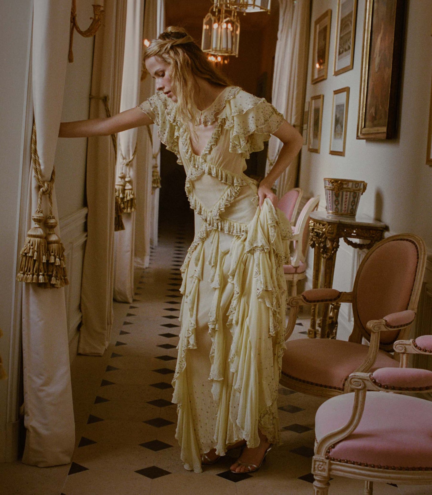 Woman in a vintage-style yellow dress standing in an elegant room with ornate decor.