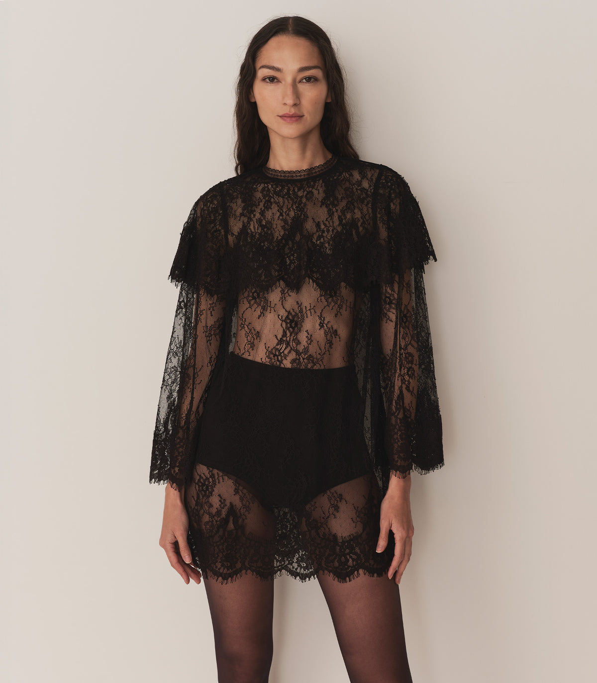 A person wearing a sheer black lace dress and sheer black tights.
