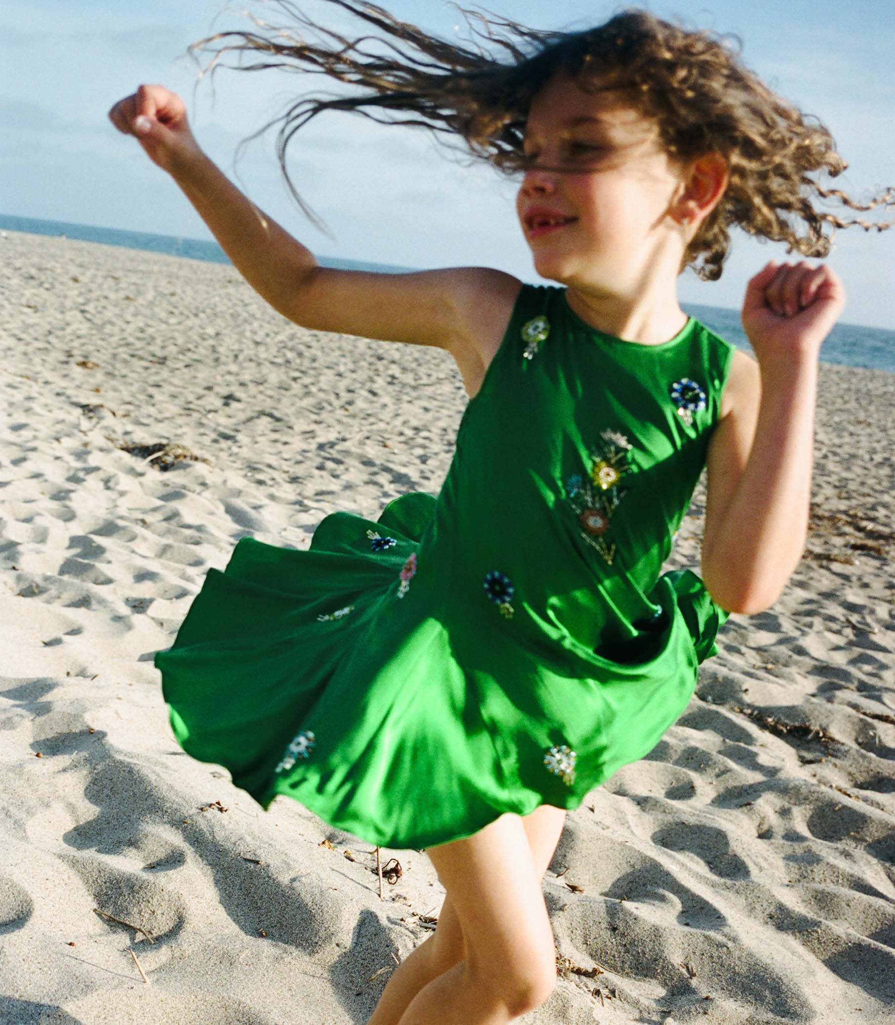 Child in a green dress running on a sandy beach 1
