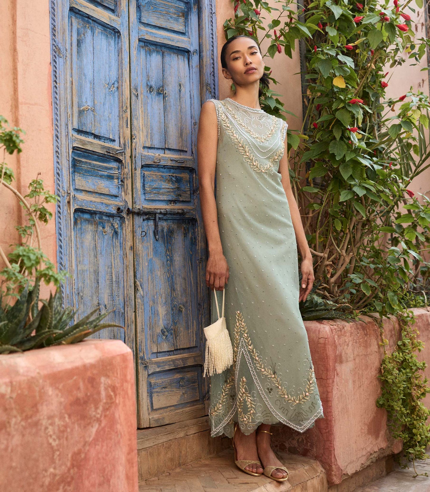 Woman in a light green dress with floral embellishments standing in front of a rustic door.