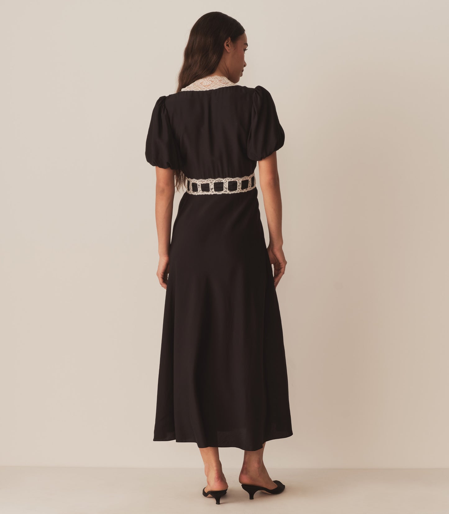 Zahara wears the Augustina Dress in Black, which features short puffed sleeves and a deep V-neckline trimmed with intricate lace.
