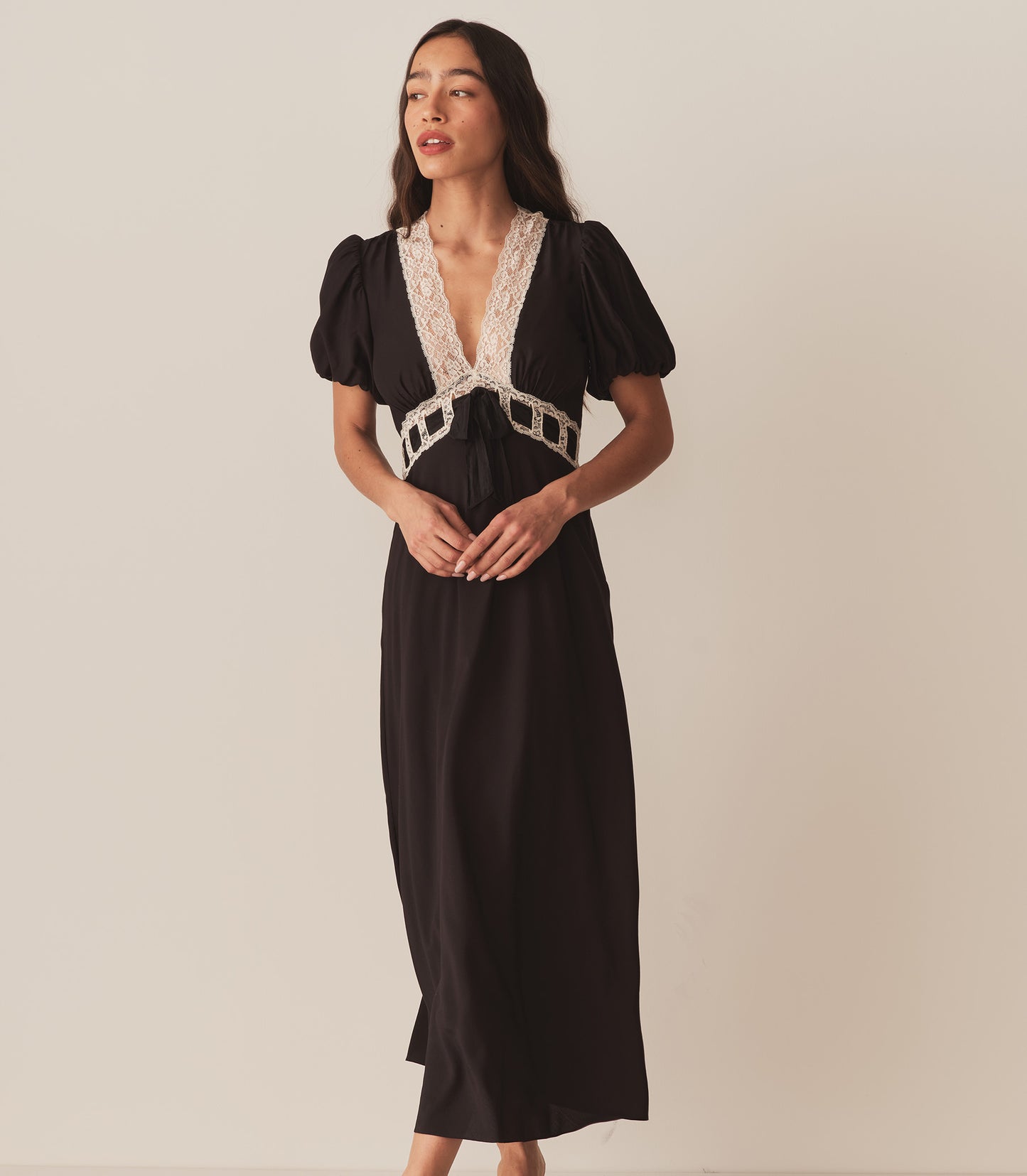 Zahara wears the Augustina Dress in Black, which features short puffed sleeves and a deep V-neckline trimmed with intricate lace.