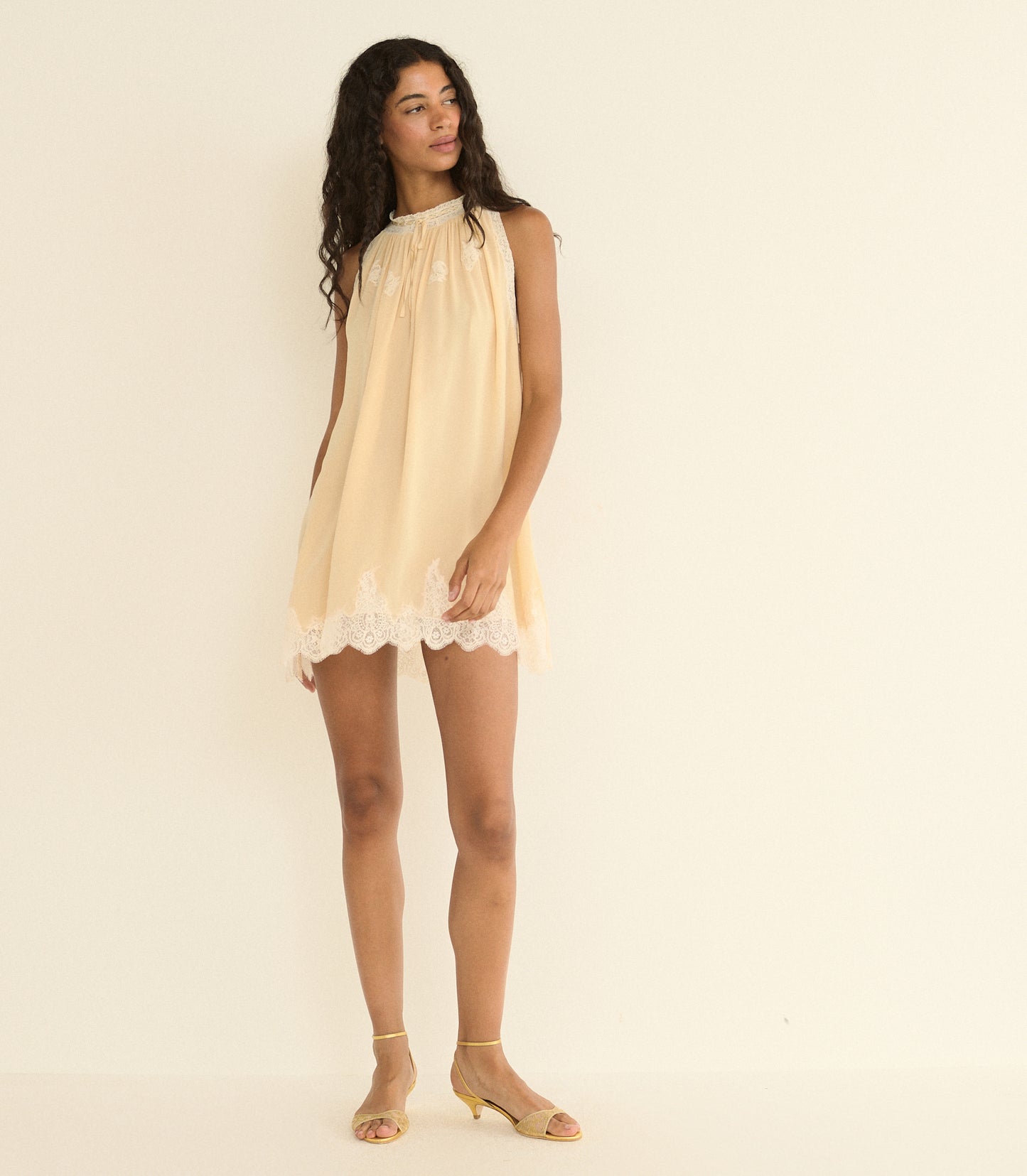 Woman wearing a light beige dress with lace trim on a plain background