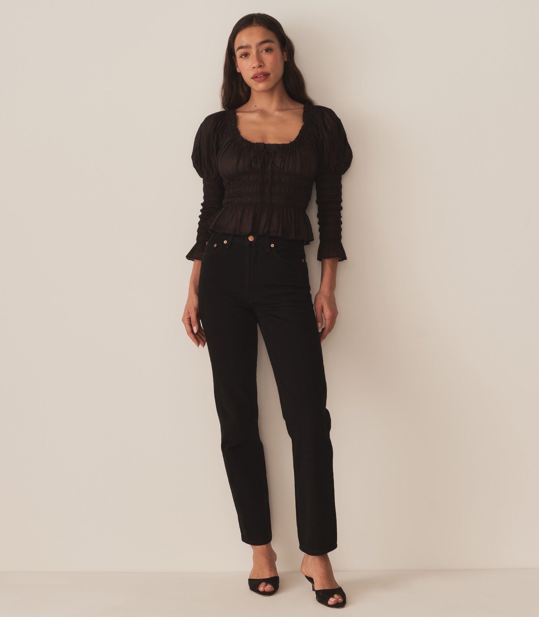 A woman wearing the Baptisia Top in Black, featuring puffed shoulders and ruching at the arms and bodice. 3