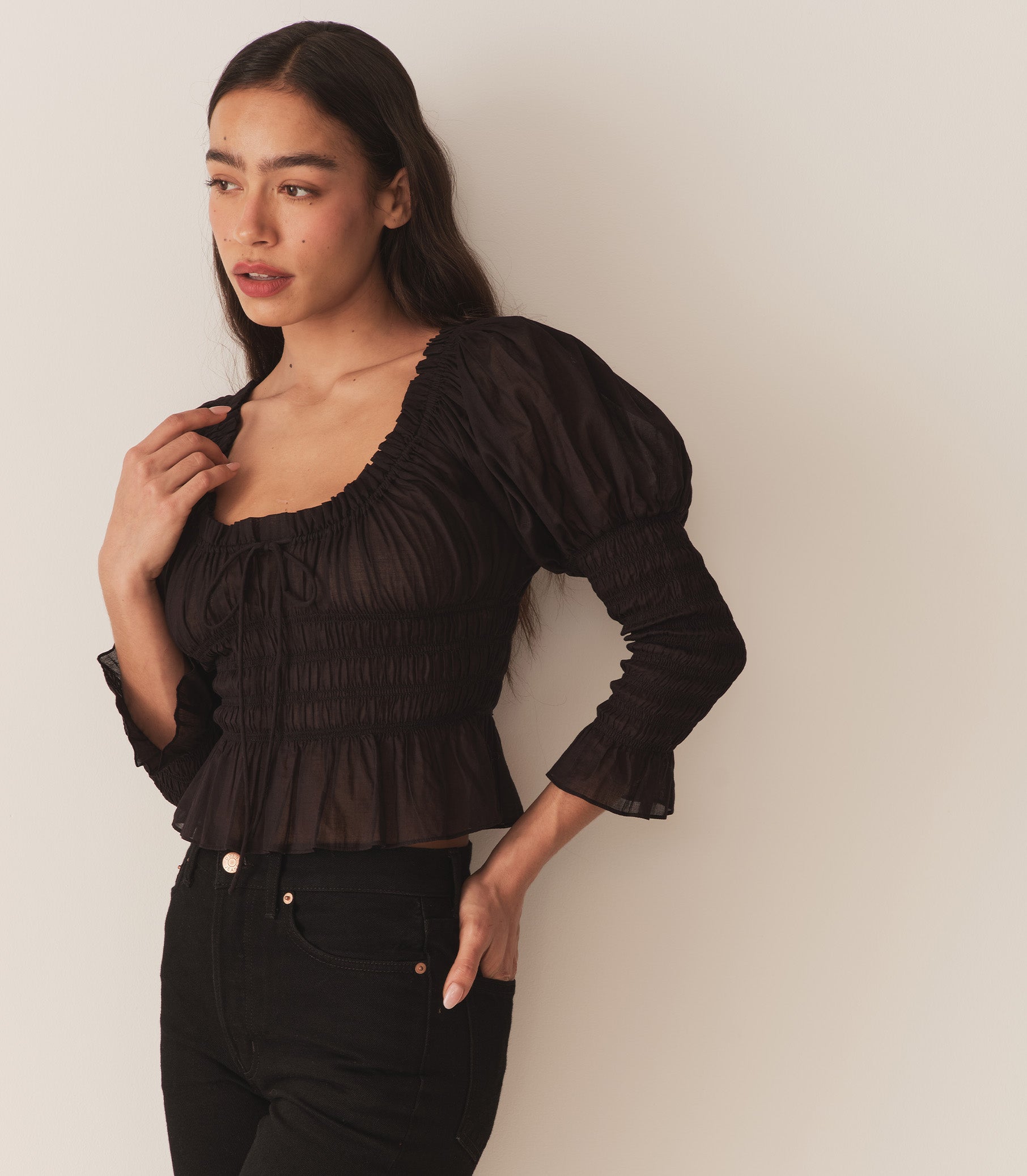 A woman wearing the Baptisia Top in Black, featuring puffed shoulders and ruching at the arms and bodice. 2
