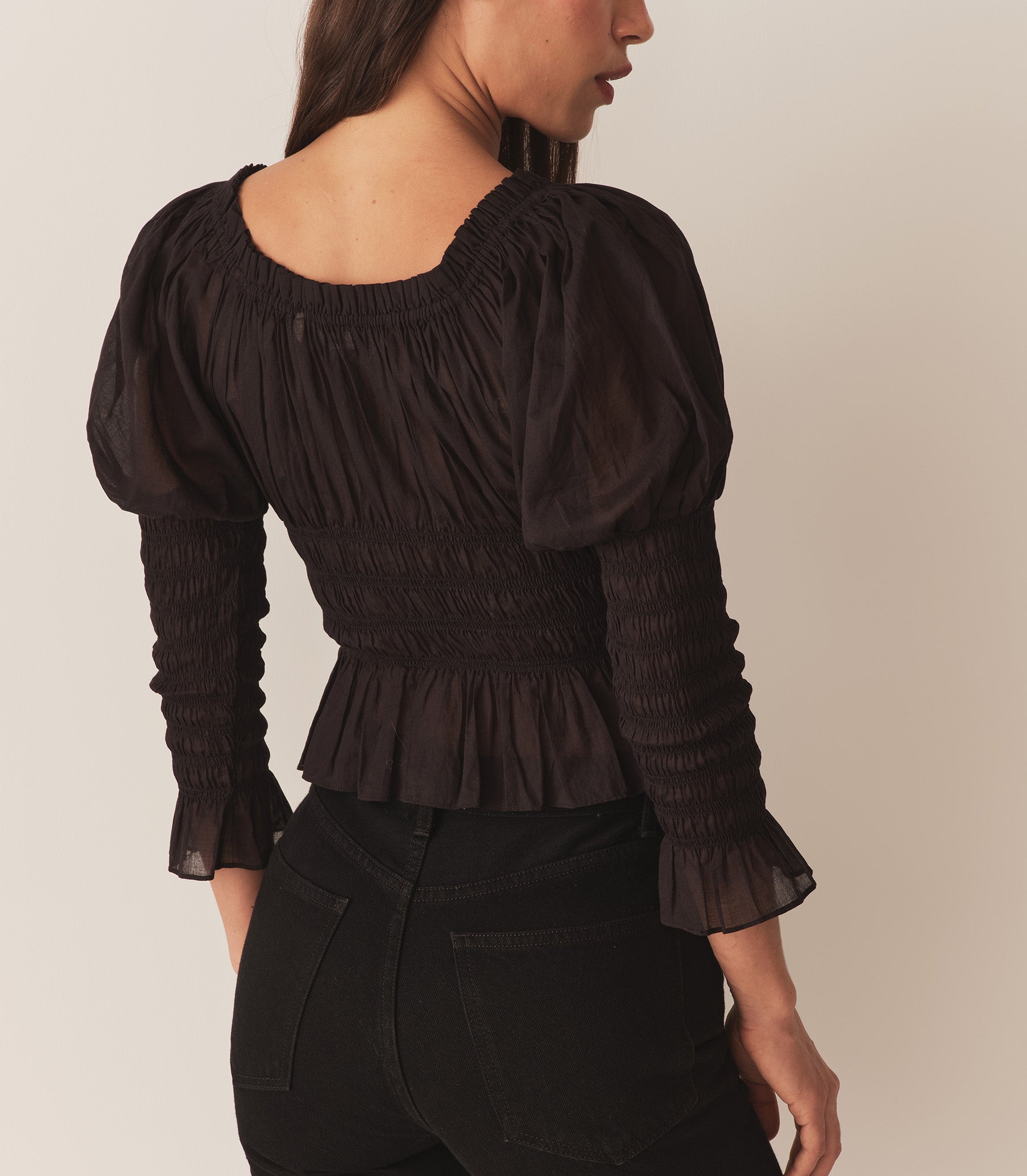 A woman wearing the Baptisia Top in Black, featuring puffed shoulders and ruching at the arms and bodice. 6