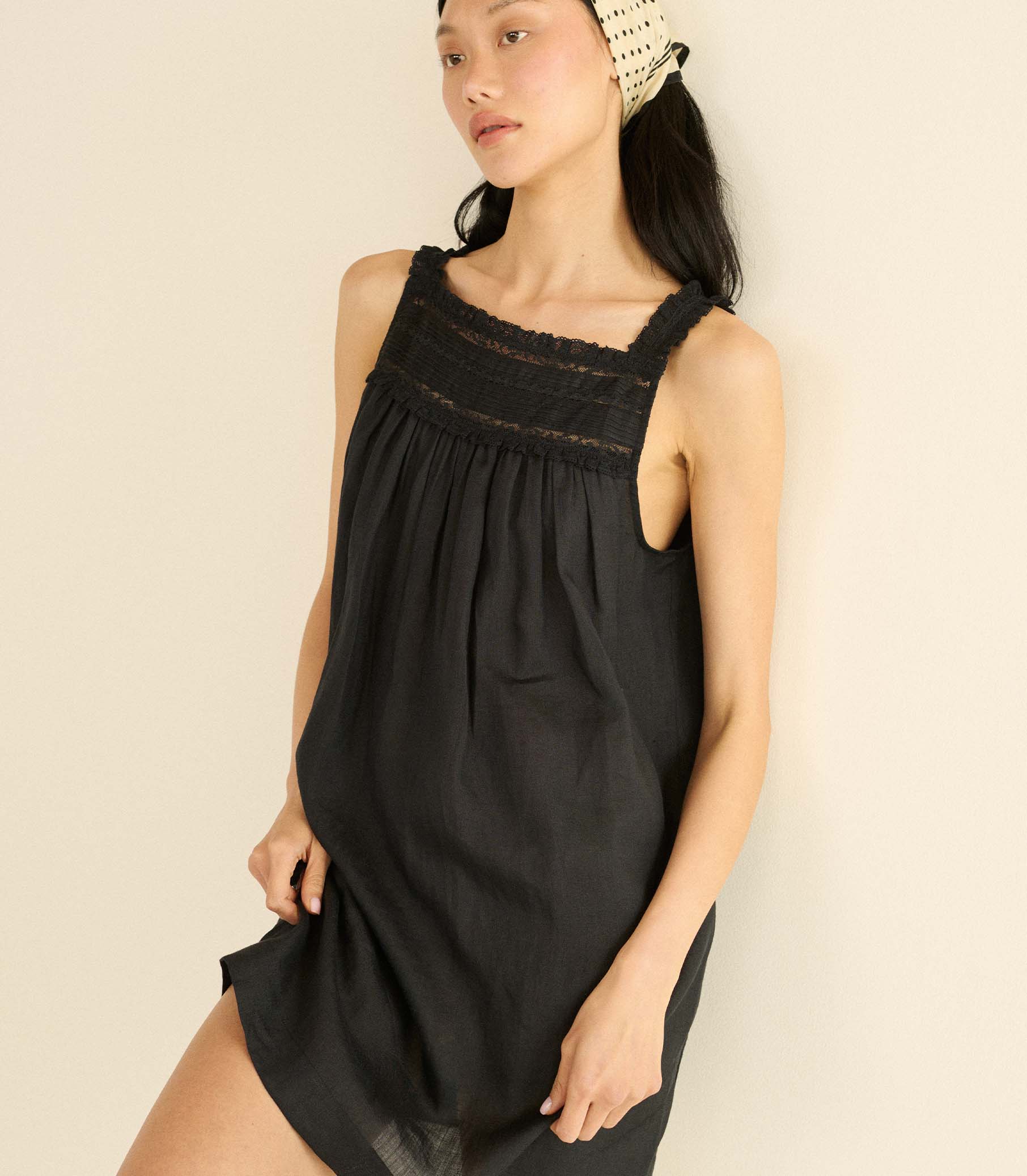 Woman wearing a black sleeveless mini dress with lace details on a beige background