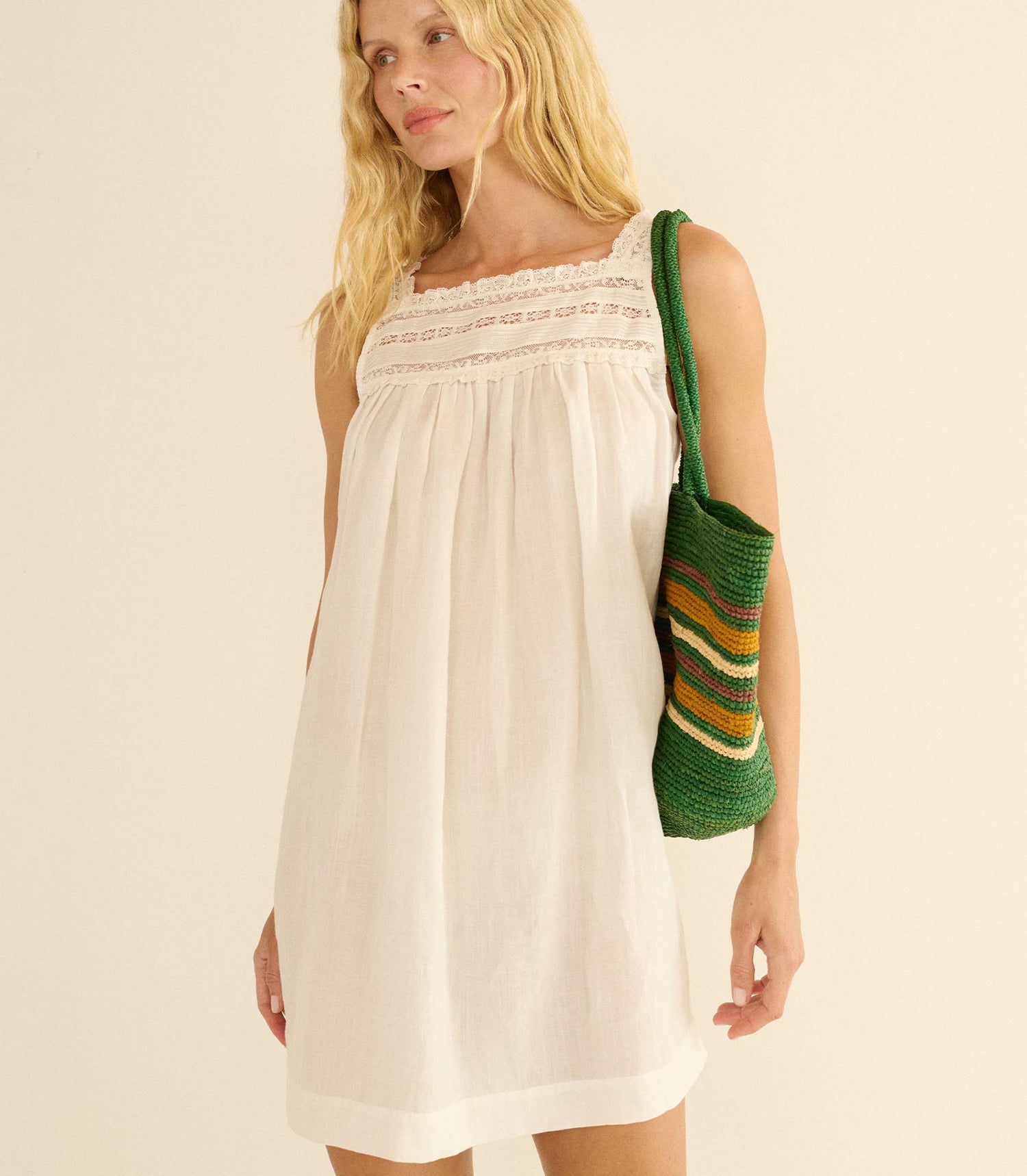 Woman wearing a white dress holding a green and brown striped bag against a beige background