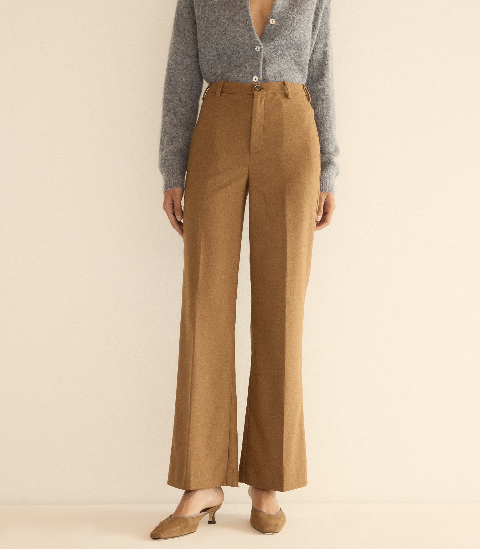Person wearing brown pants and a gray cardigan on a beige background