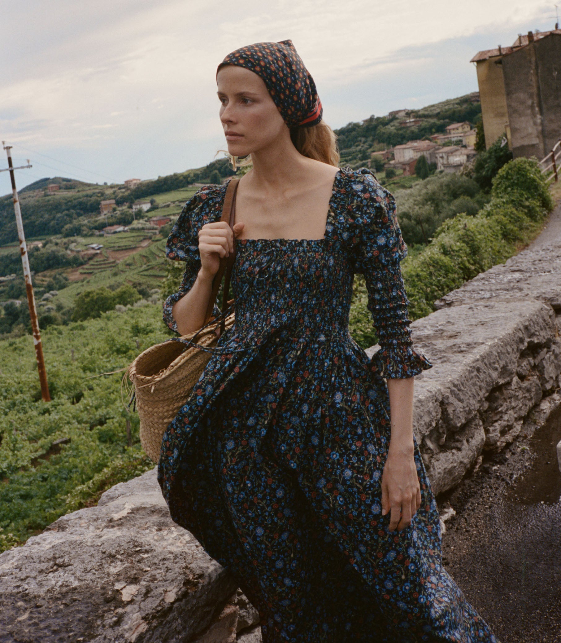 Woman in a floral dress standing on a stone wall with a scenic background 3