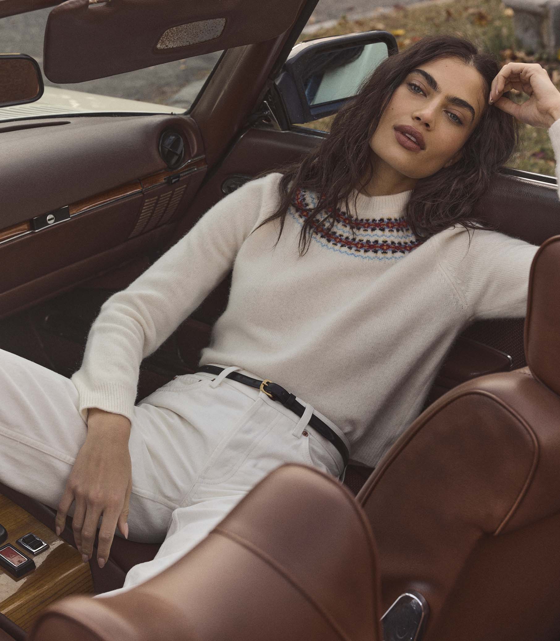 Woman wearing a cream fair isle sweater, sitting inside a vintage car with a brown interior 1

