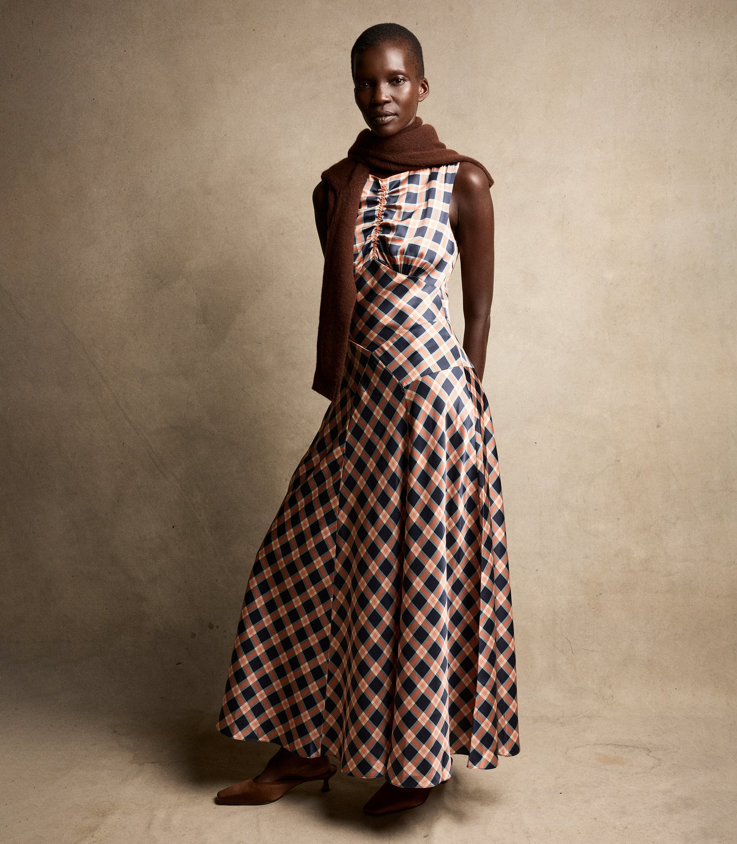 Woman wearing a long, patterned dress with a brown top against a neutral background