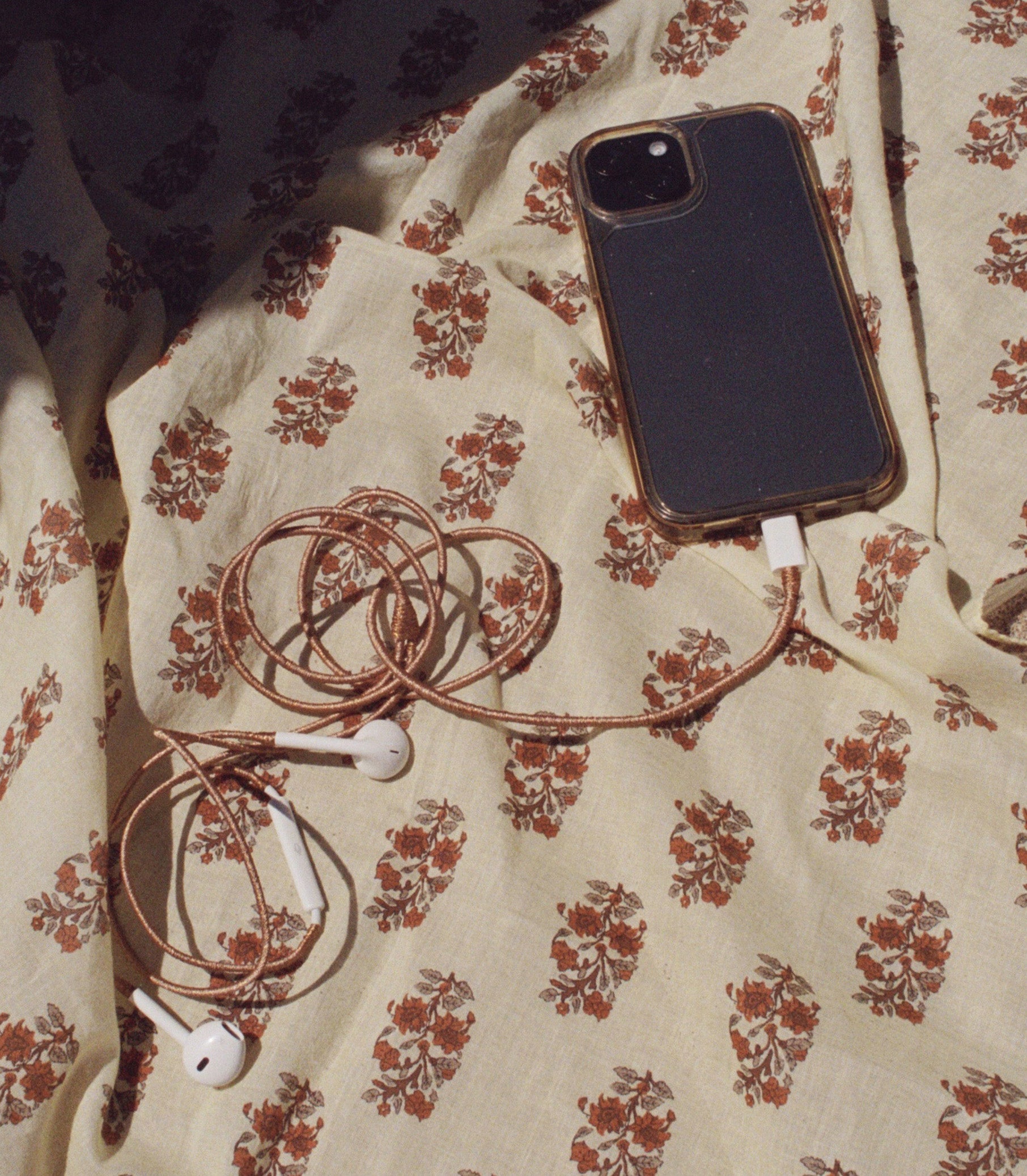 Cellphone with copper earphones on a floral blanket