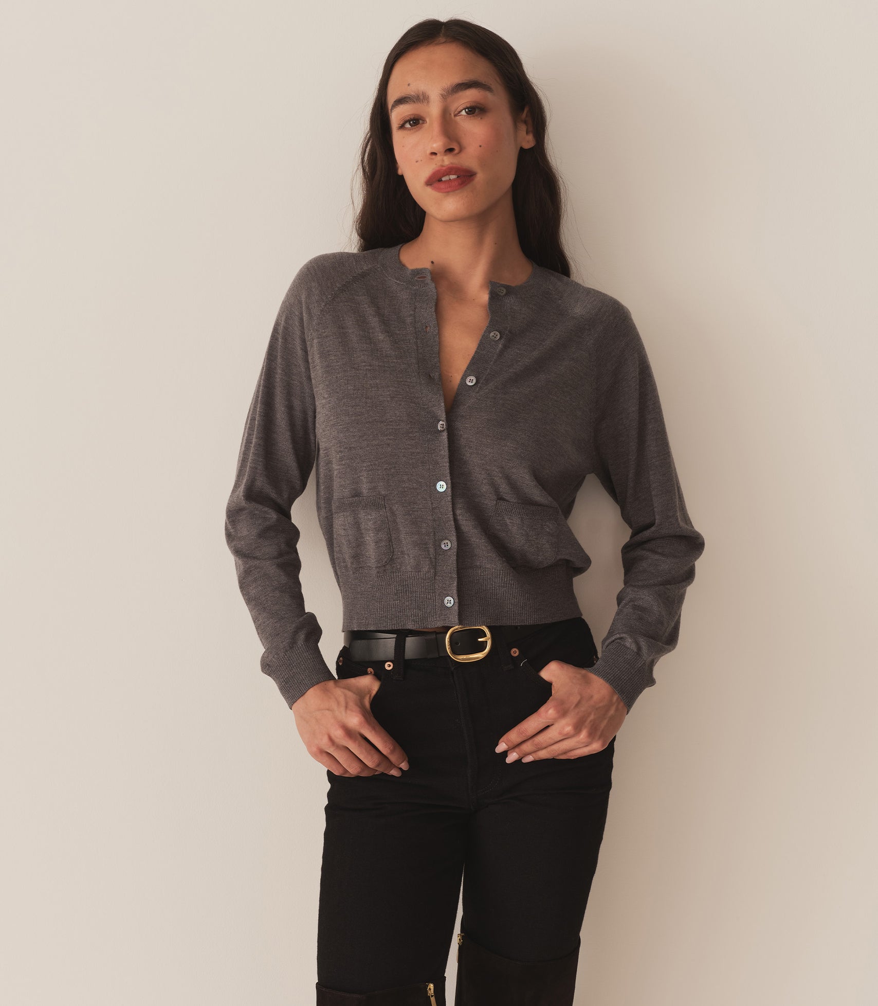 Zahara wears a grey cardigan with black pants and a belt.