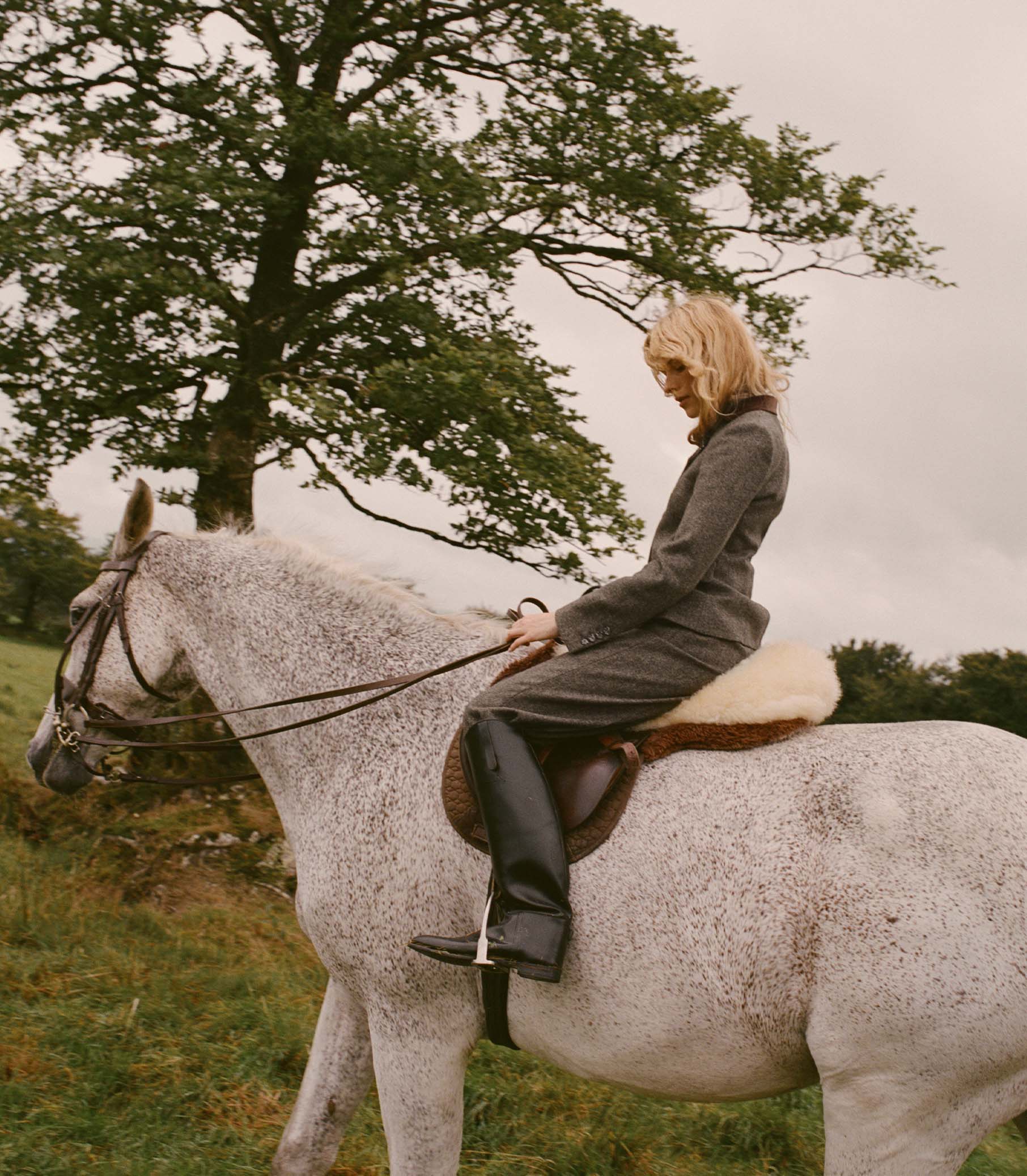 Woman riding a white horse in a matching grey suit set.