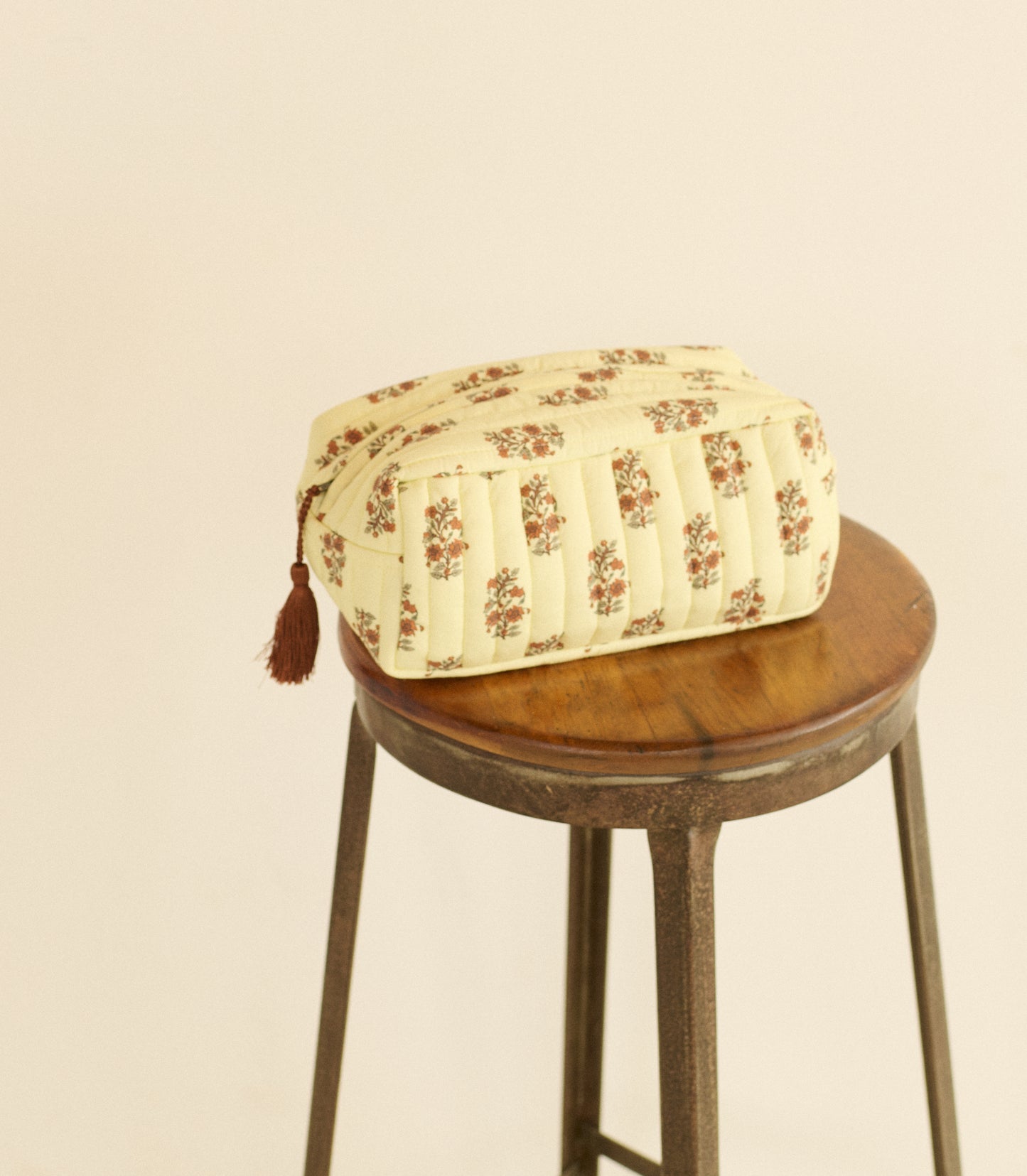Floral-patterned bag with a tassel on a wooden stool against a beige background