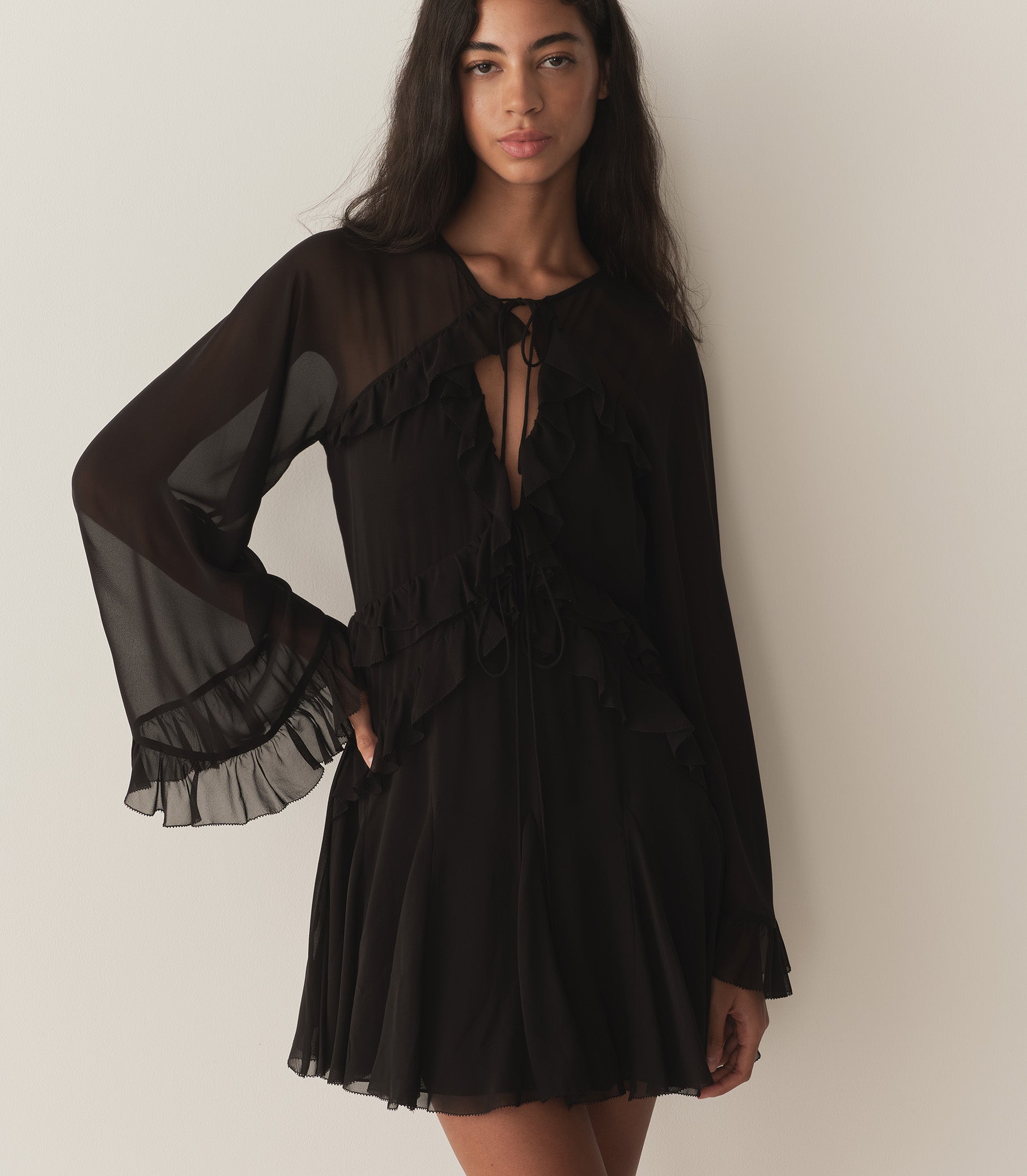 Rocio is wearing a black mini dress with ruffle details and long sleeves, paired with black kitten heels.