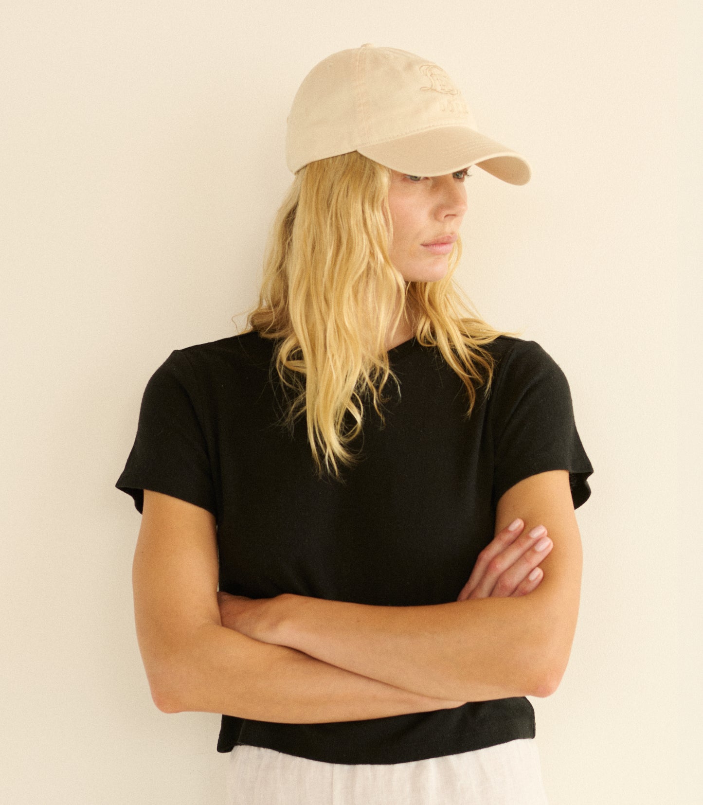 Woman wearing a black t-shirt and beige cap against a plain background