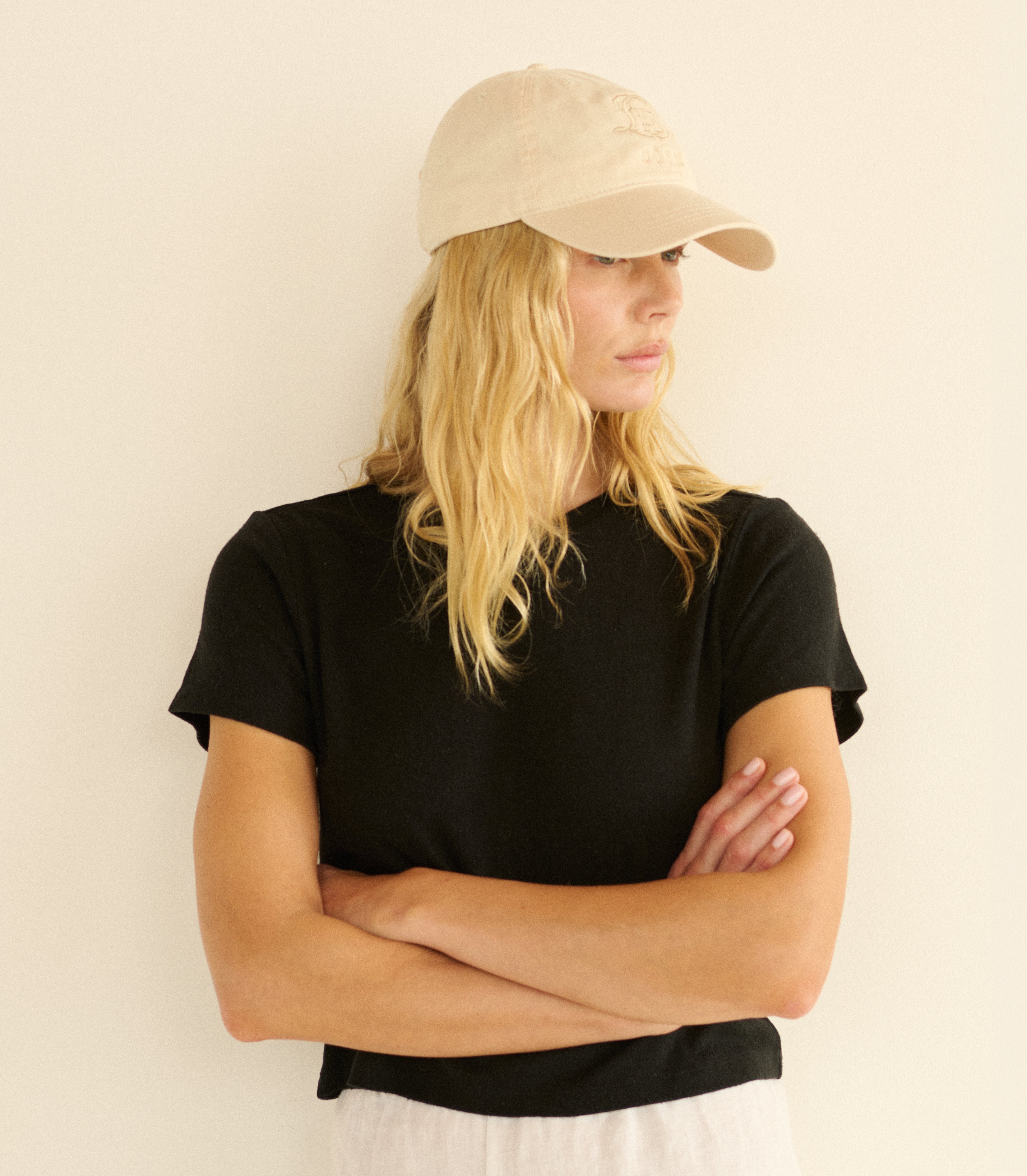 Woman wearing a black t-shirt and beige cap against a plain background