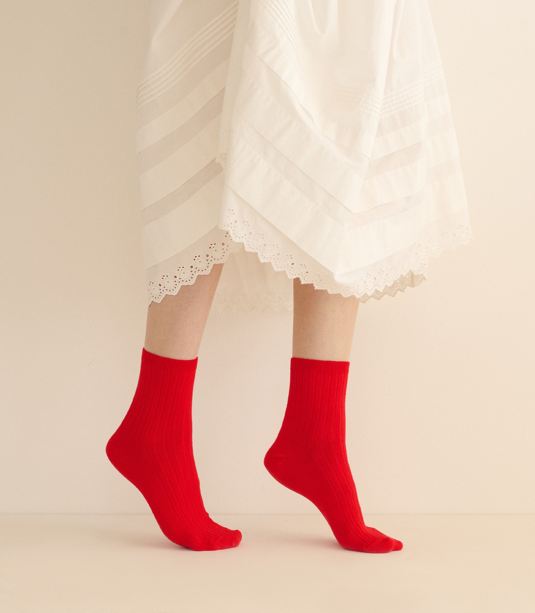 Red socks worn with a white lace dress on a beige background 1