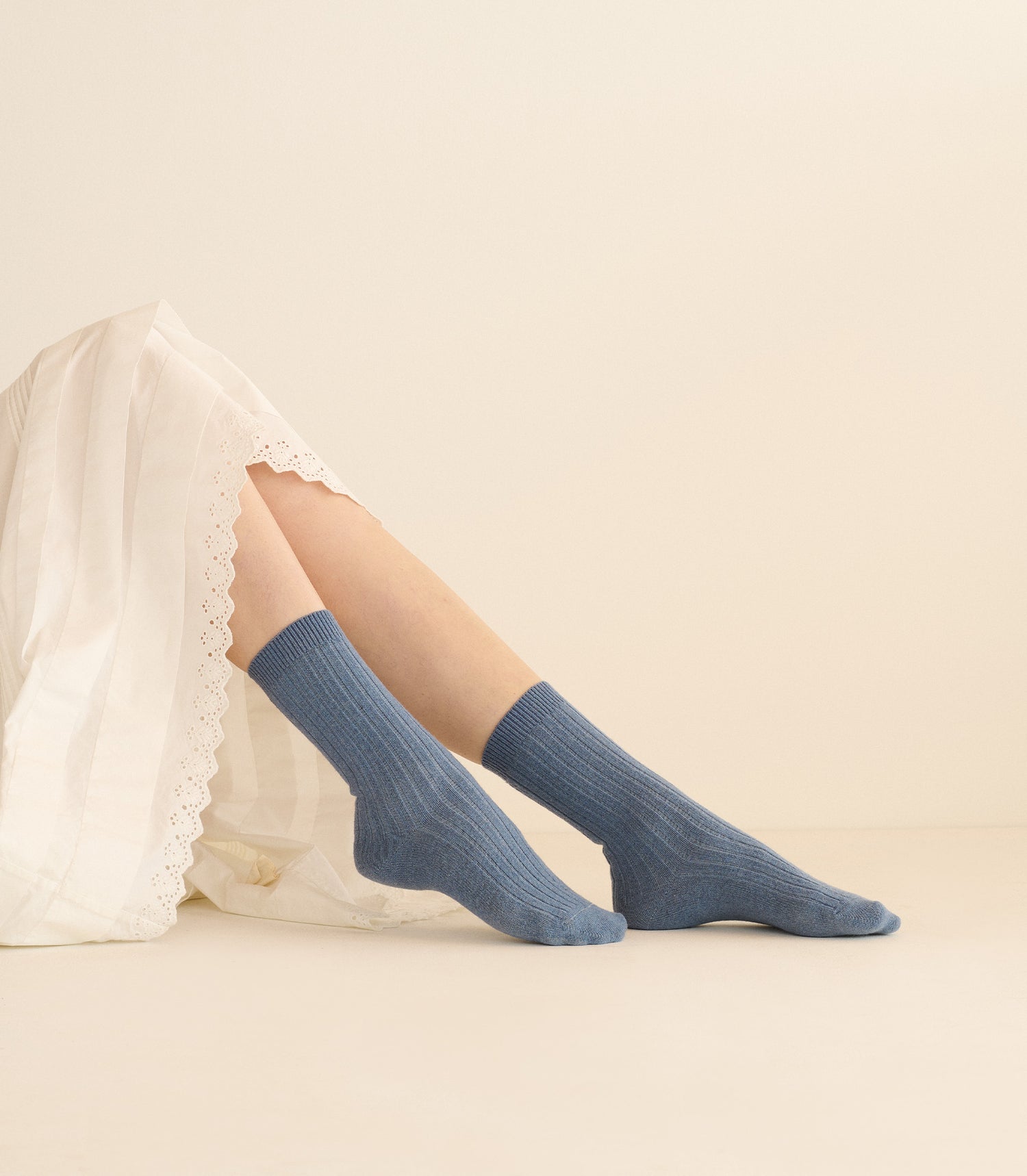 Blue socks worn with a white lace garment on a beige background