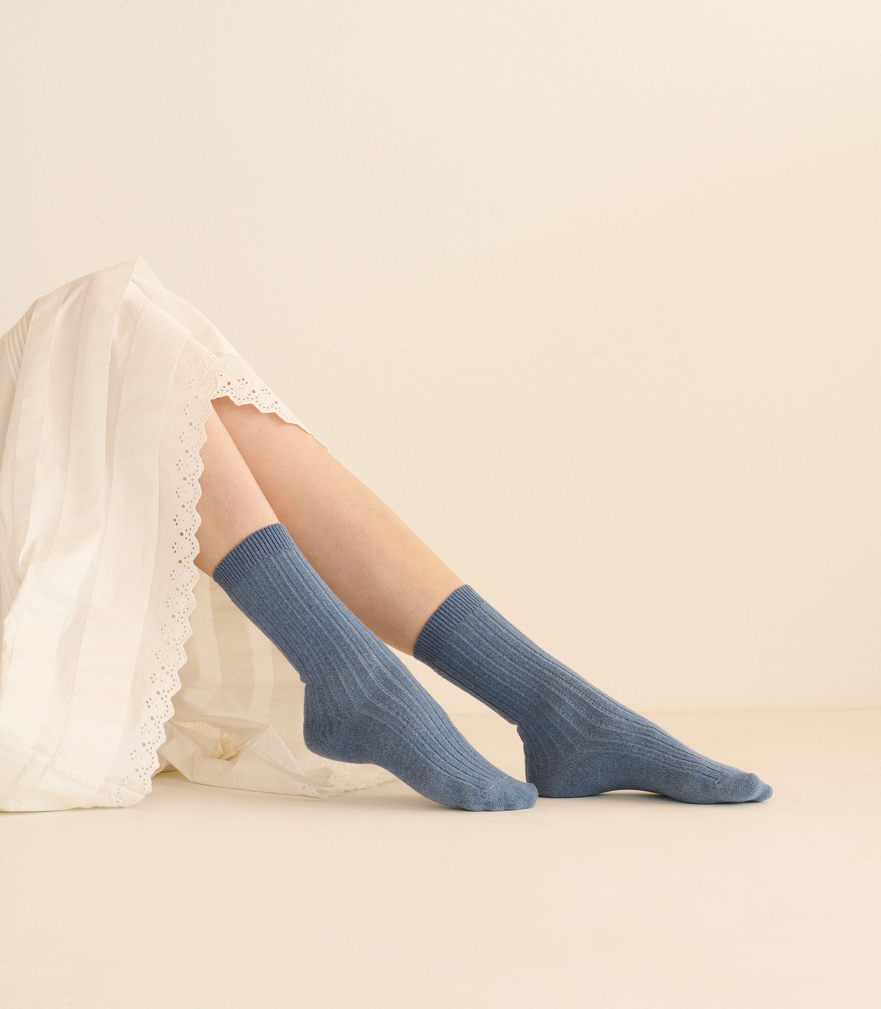 Blue socks worn with a white lace garment on a beige background 1