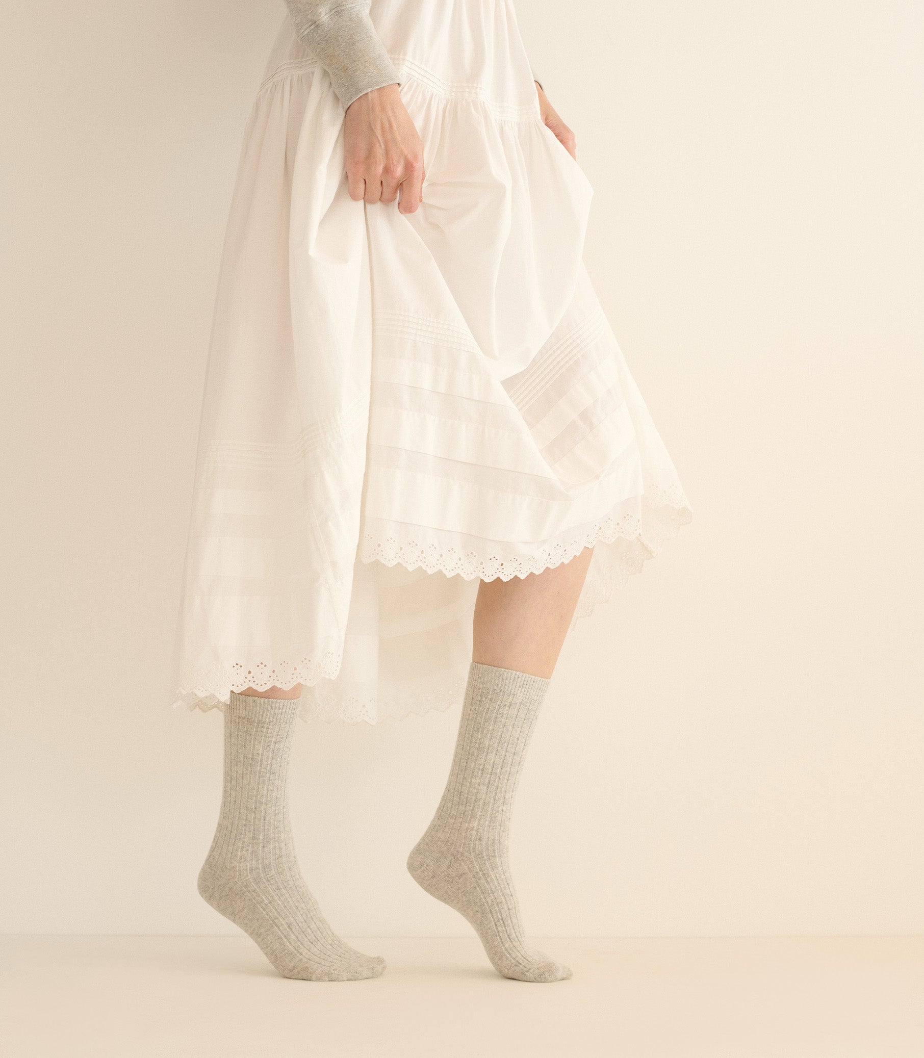 Person wearing a white dress with lace details and gray socks on a plain background 1