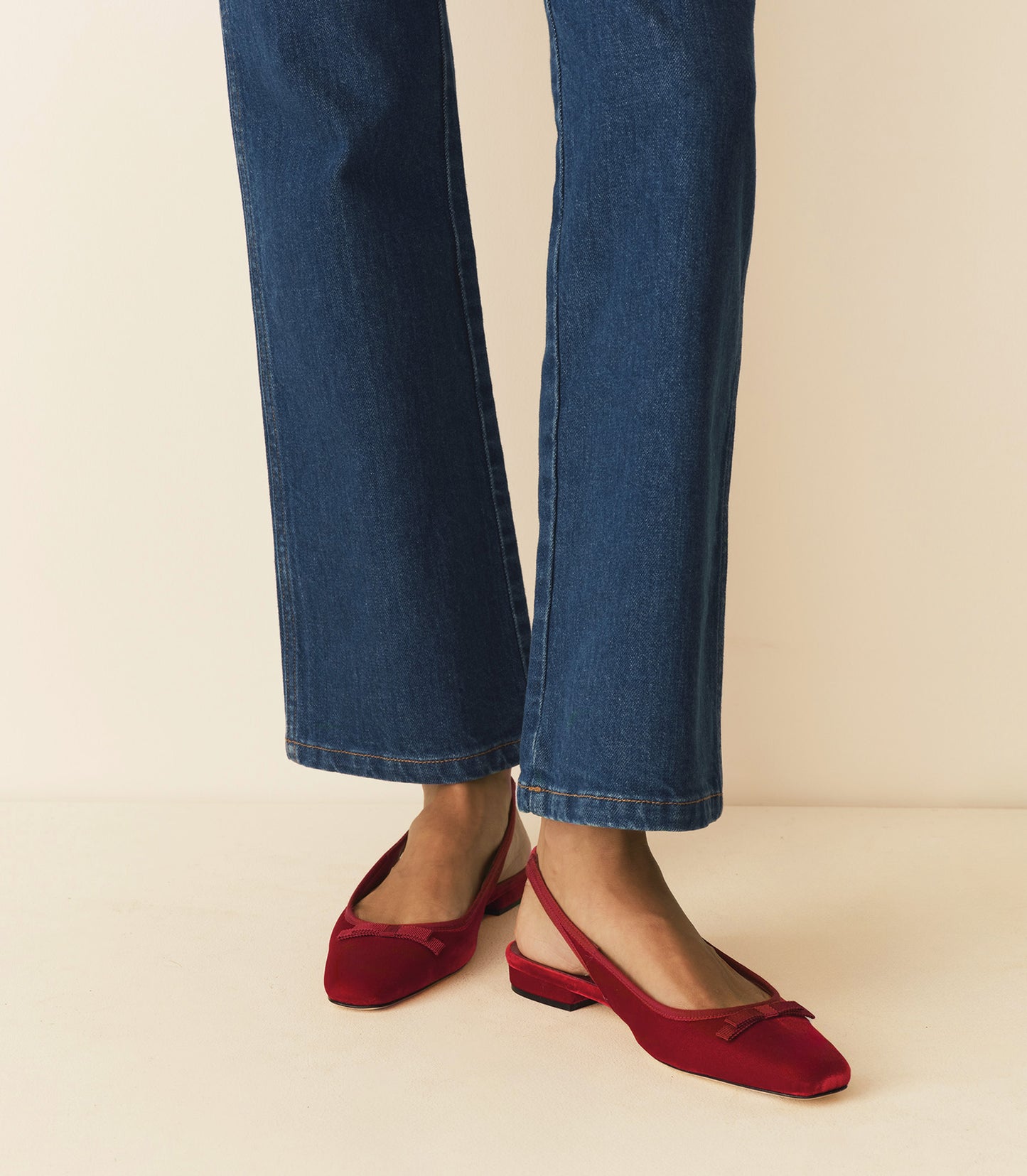 Person wearing blue jeans and red shoes on a beige background