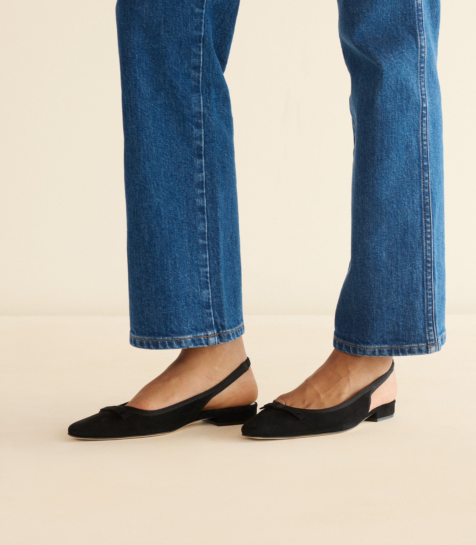 Person wearing blue jeans and black flats on a beige background 1