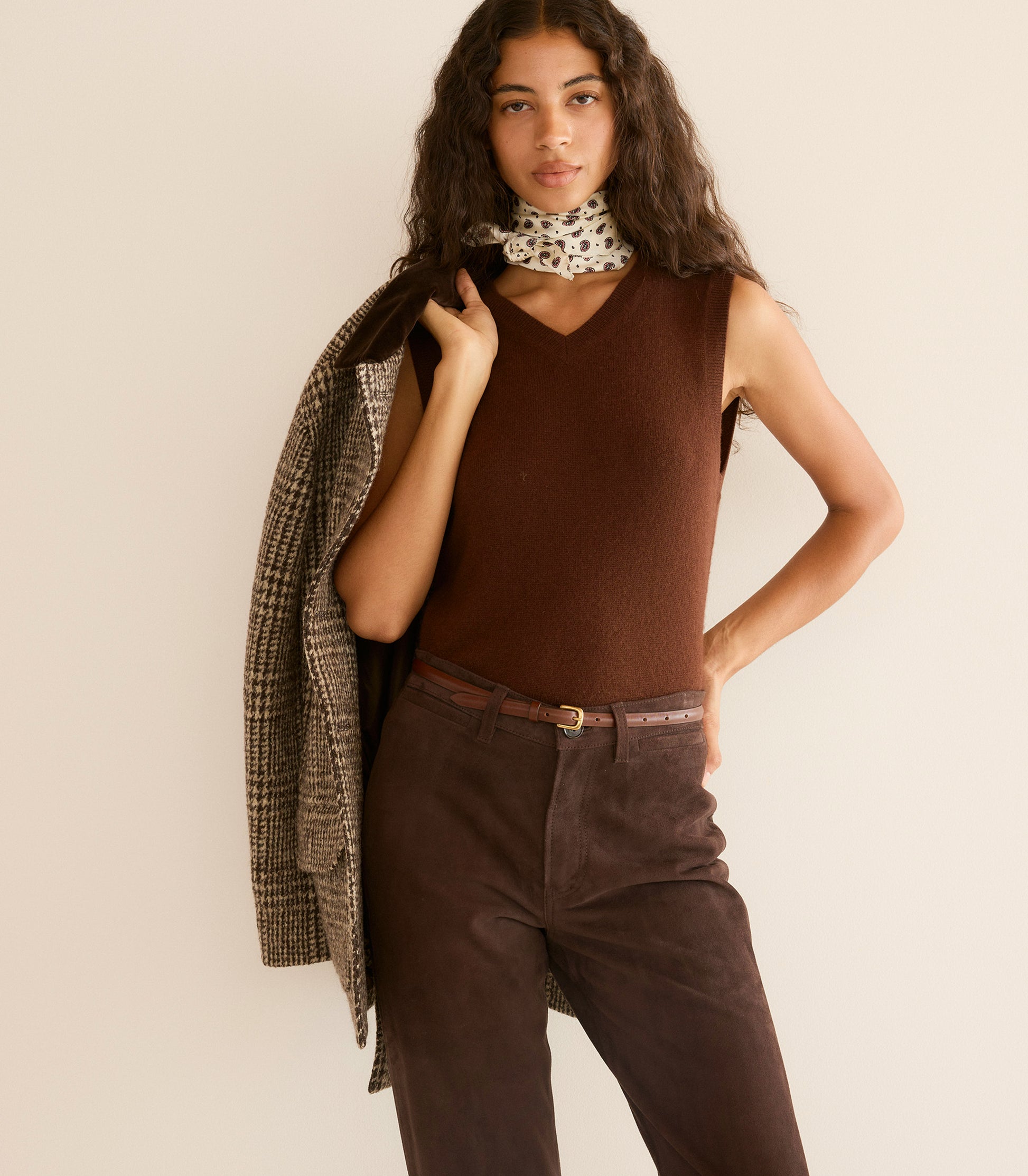 Woman wearing a brown sleeveless top and pants with a patterned scarf on a beige background 1