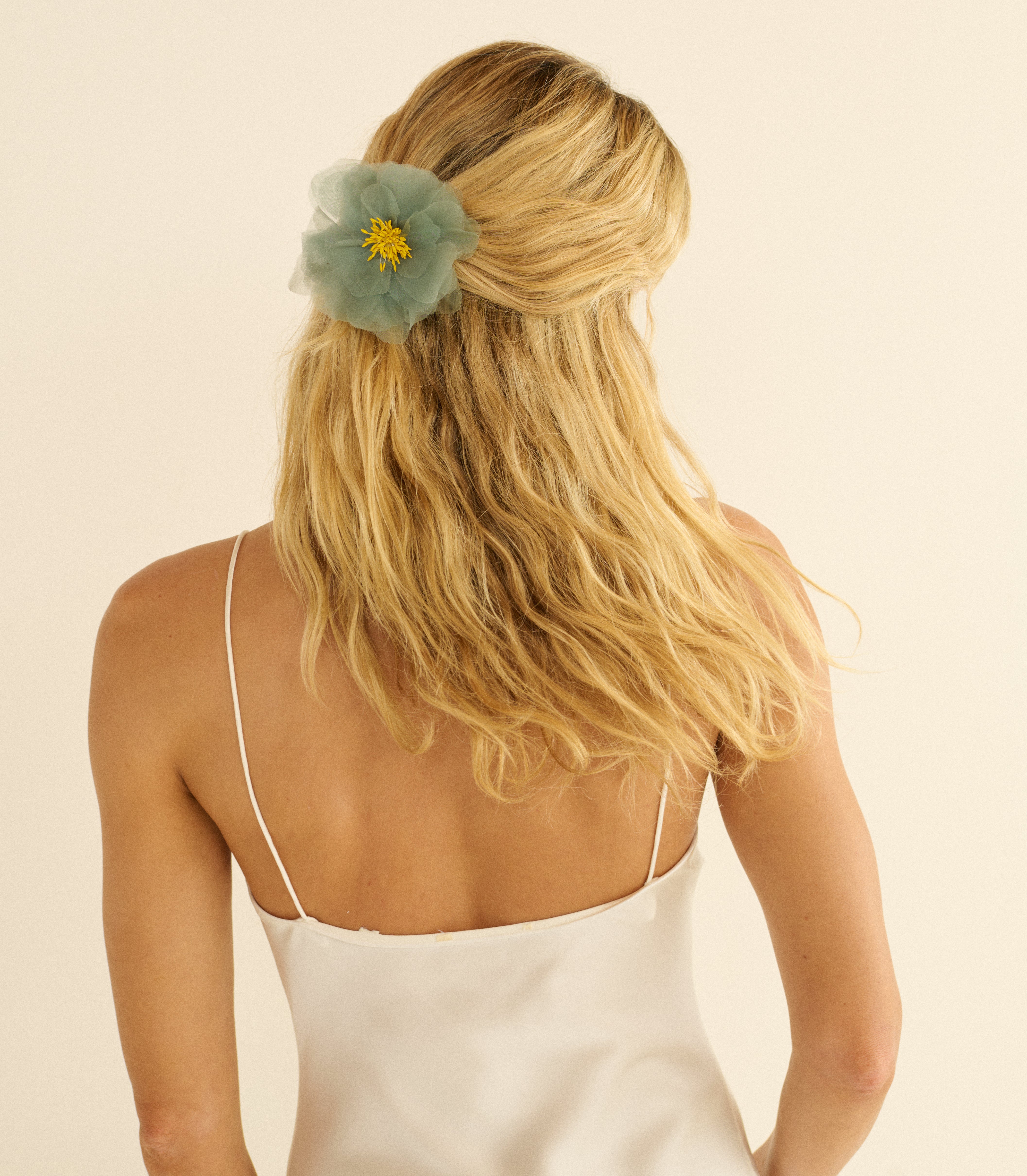 Woman with blonde hair wearing a teal floral hair accessory against a beige background
