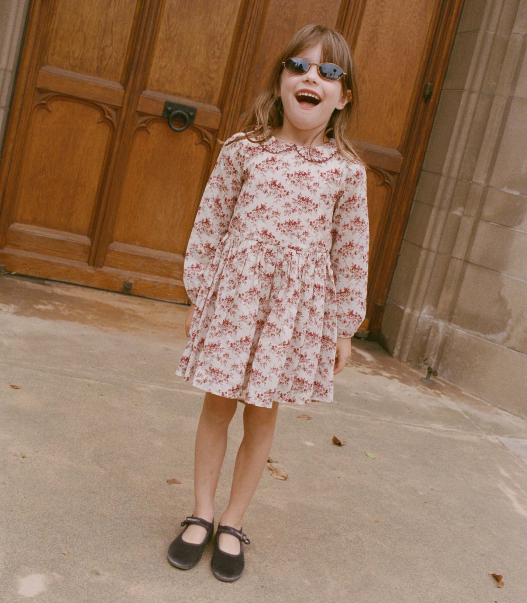 Young girl in a floral dress standing in front of a wooden door 3