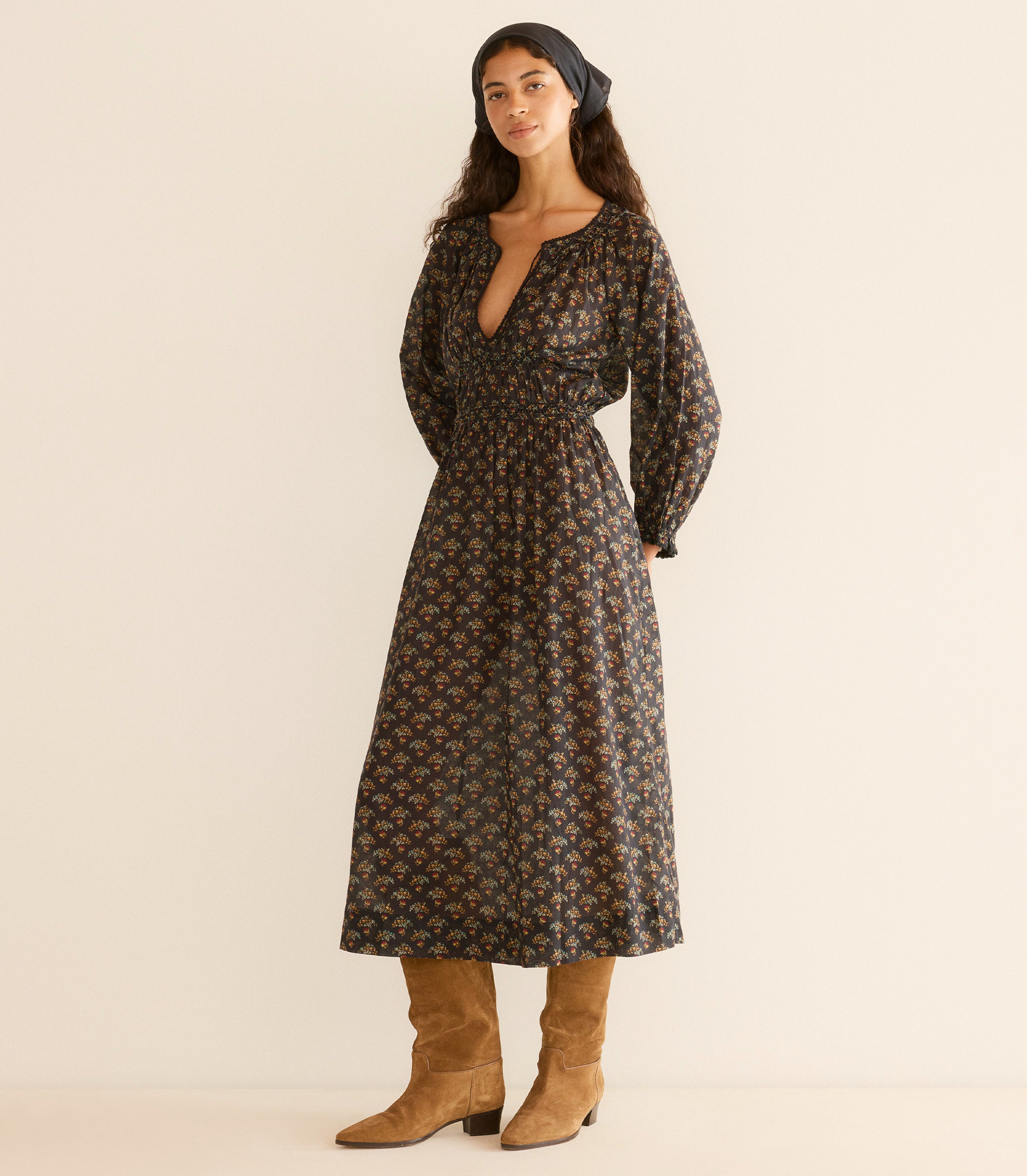 Woman wearing a floral dress with long sleeves, standing against a plain background.