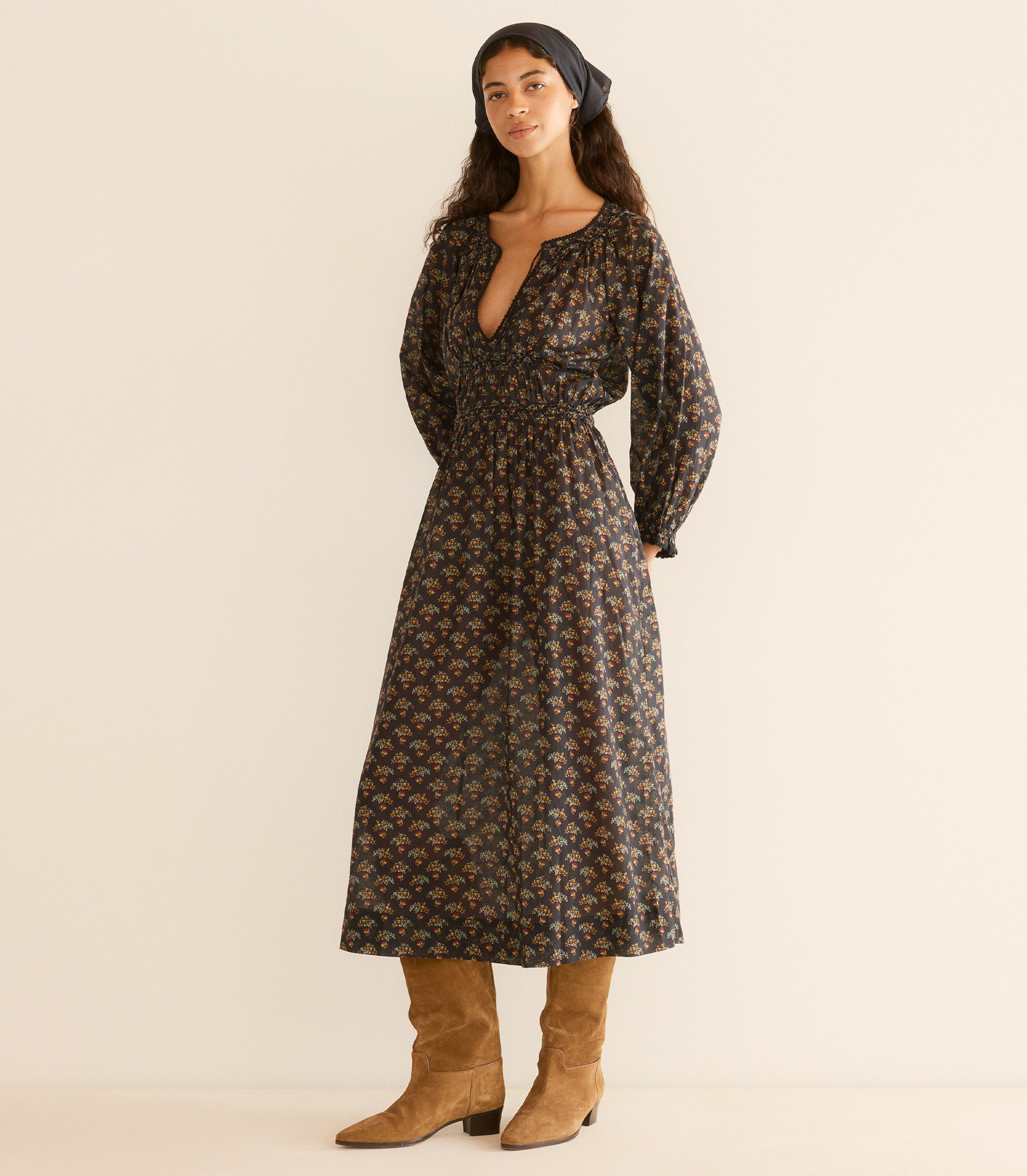 Woman wearing a floral dress with long sleeves, standing against a plain background.