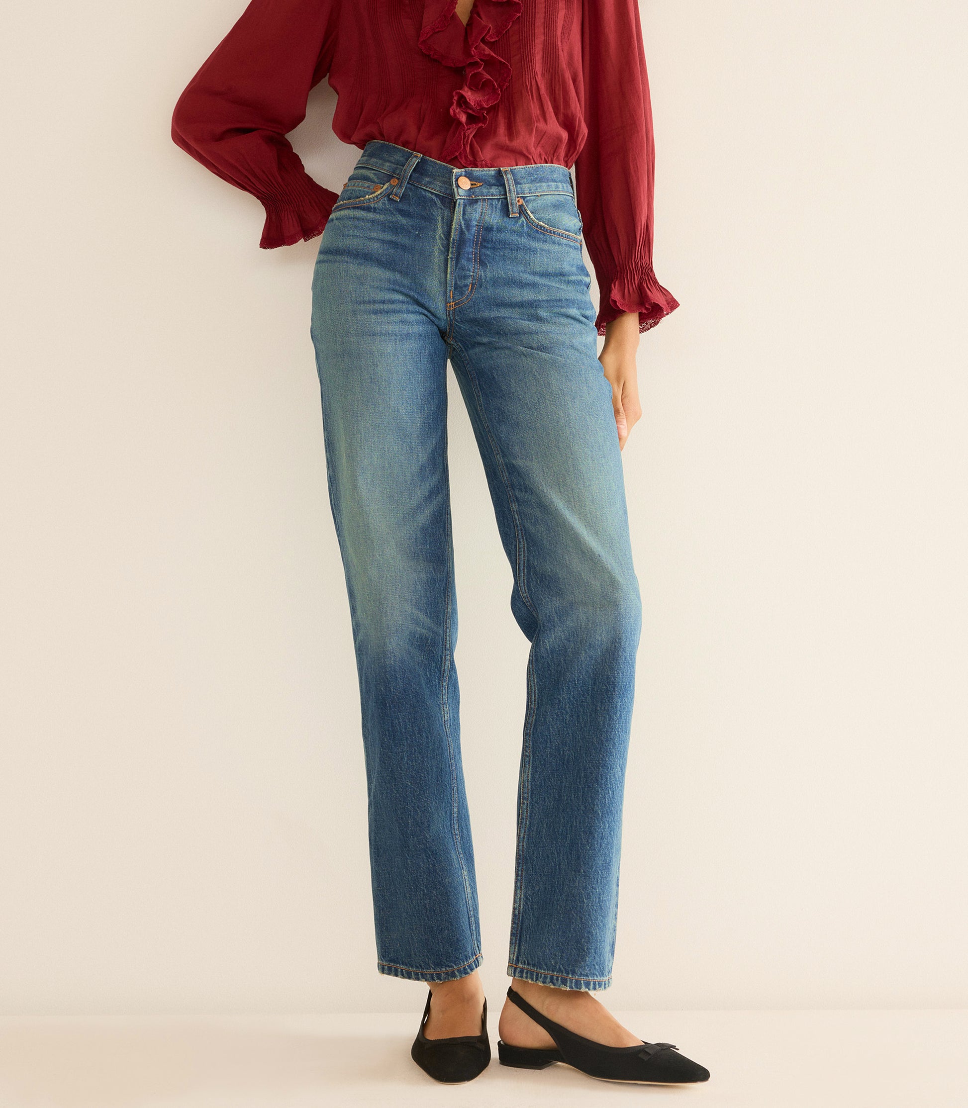 Person wearing blue jeans and a red blouse on a beige background 1