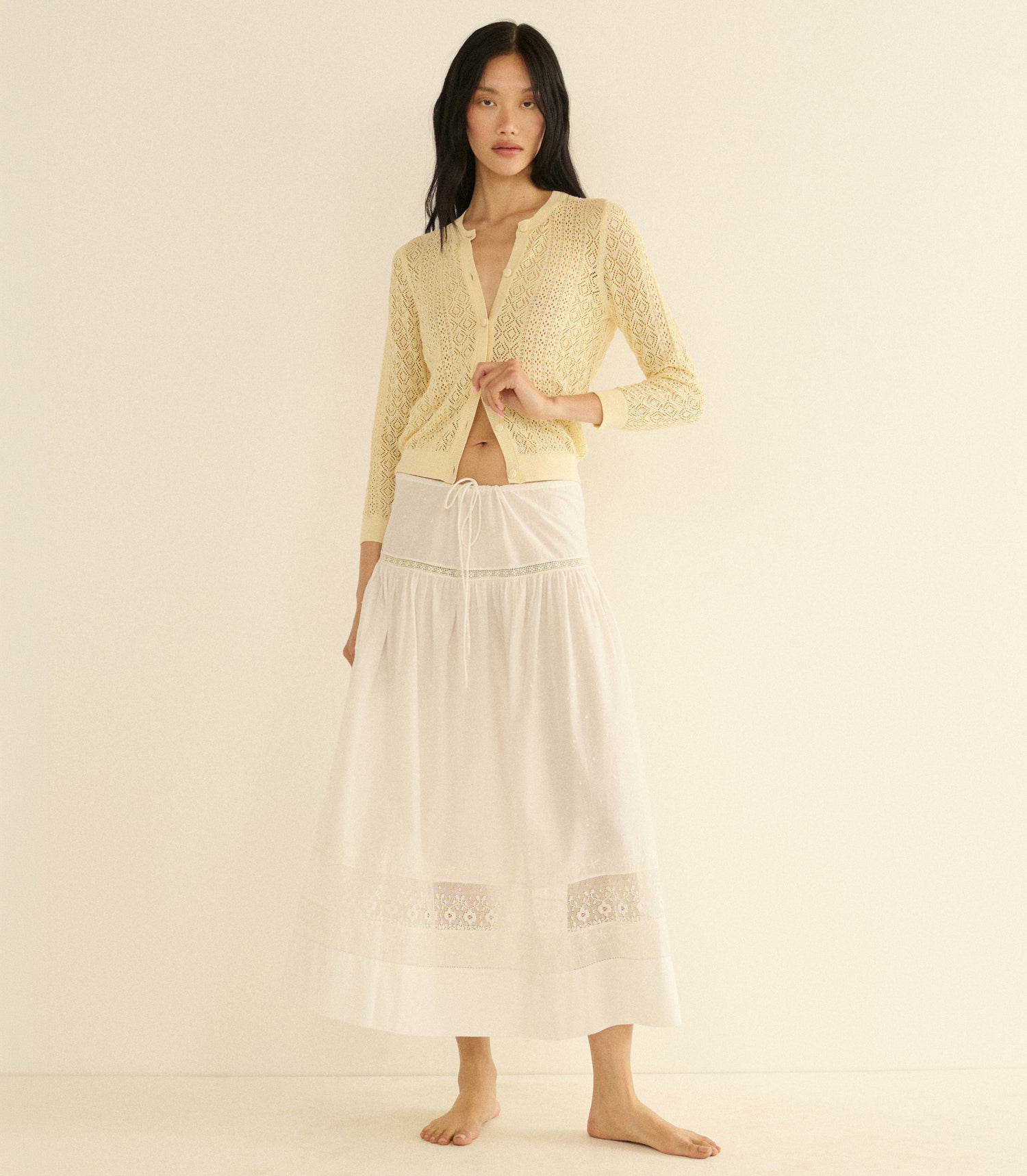 Woman wearing a cream cardigan and a white skirt on a beige background