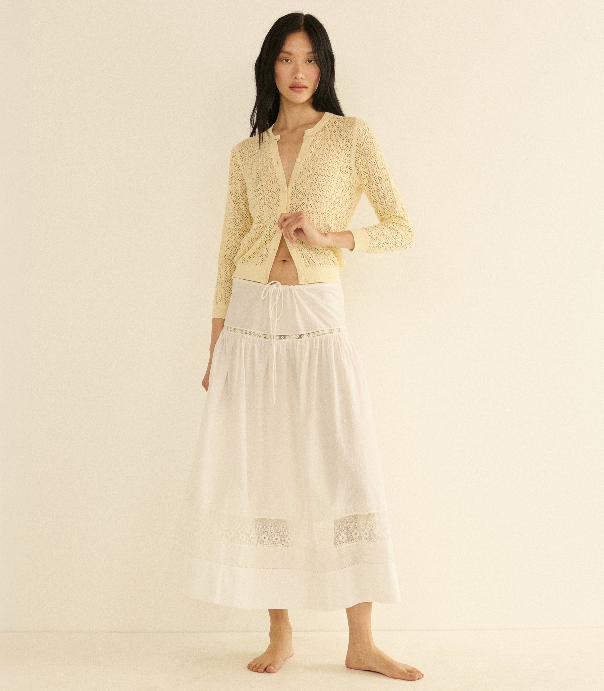 Woman wearing a cream cardigan and a white skirt on a beige background 2
