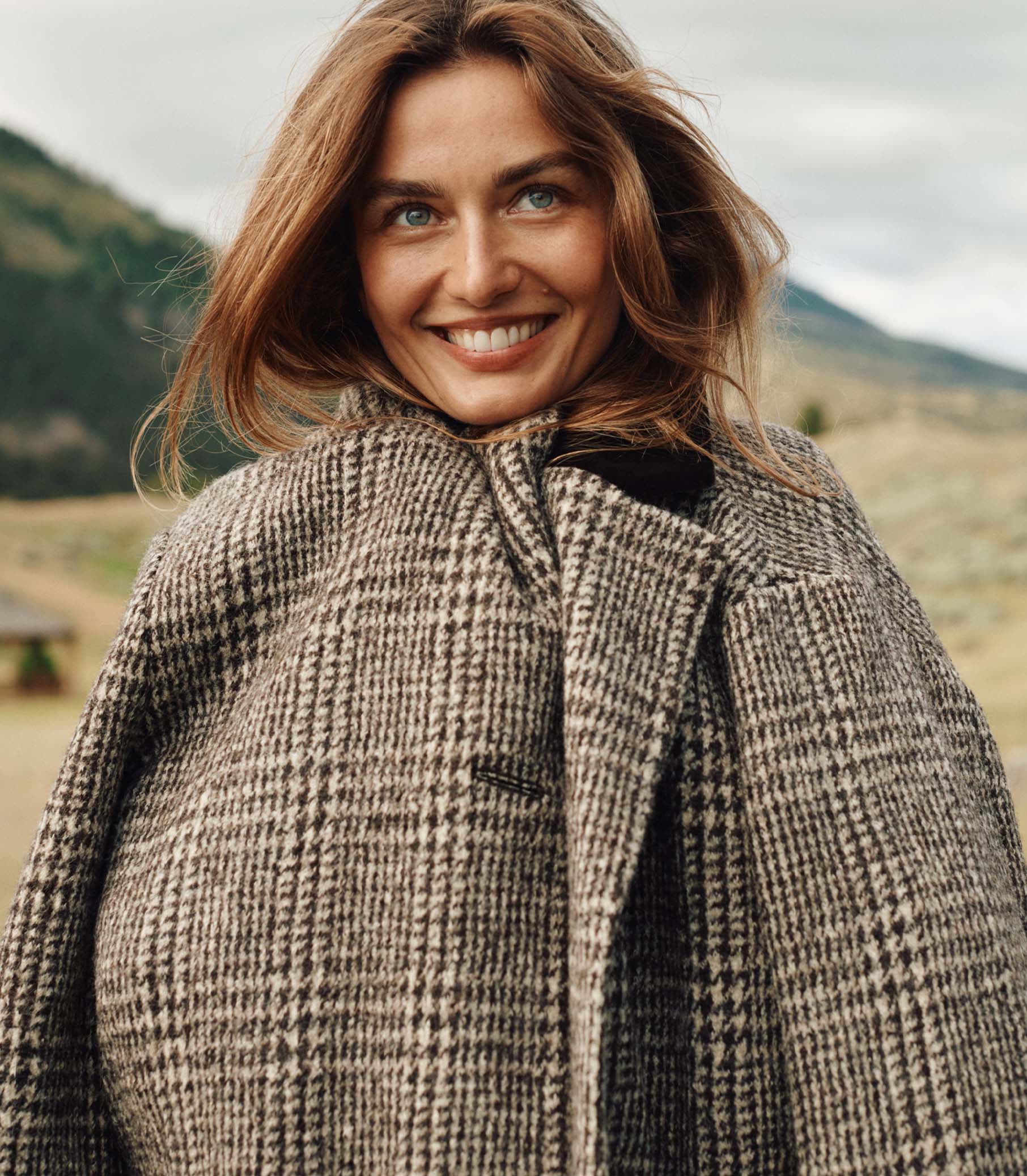 Woman wearing a checkered coat with a mountainous landscape in the background 2