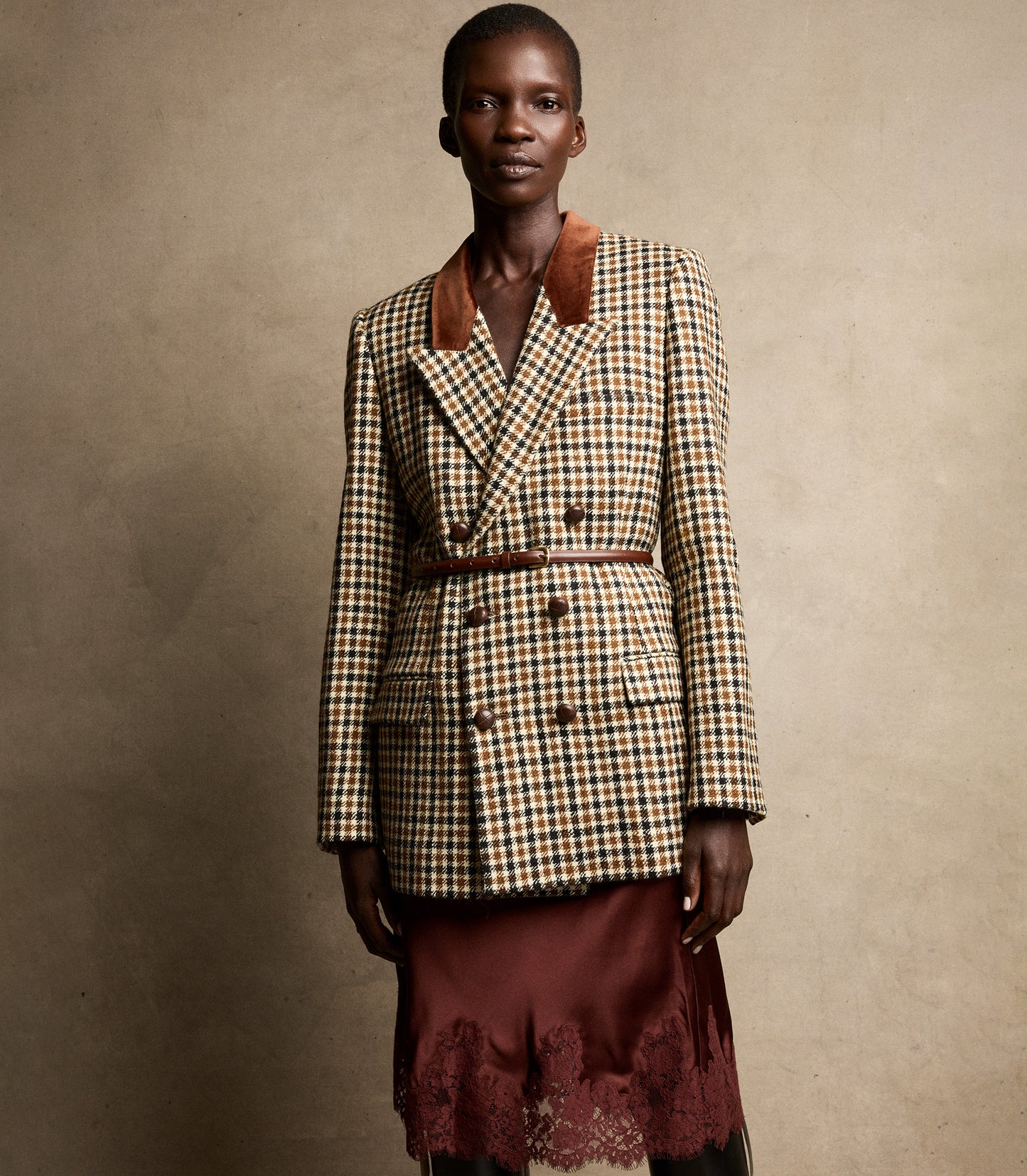 Model wearing a plaid blazer and burgundy skirt against a beige background