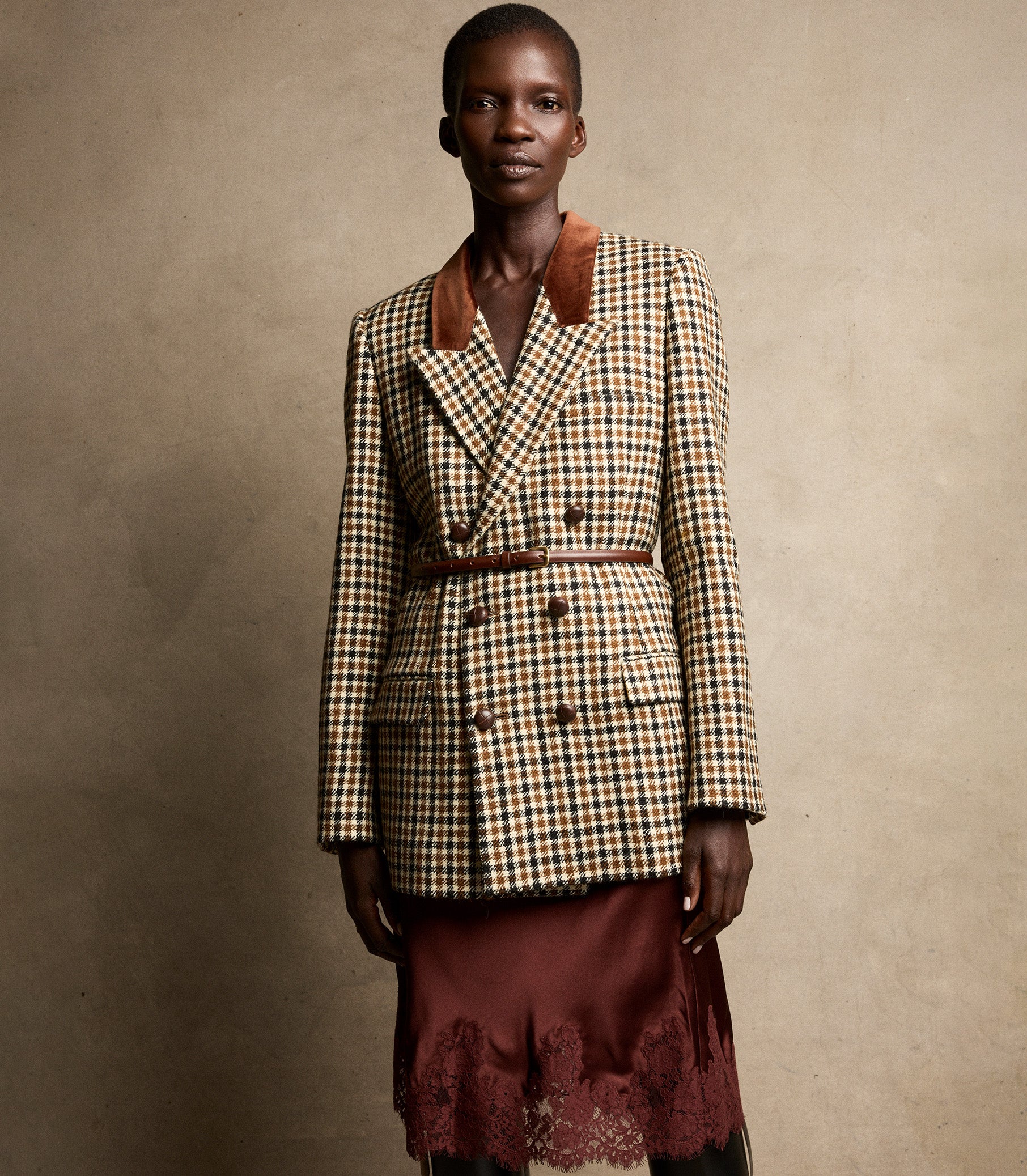 Model wearing a plaid blazer and burgundy skirt against a beige background 2