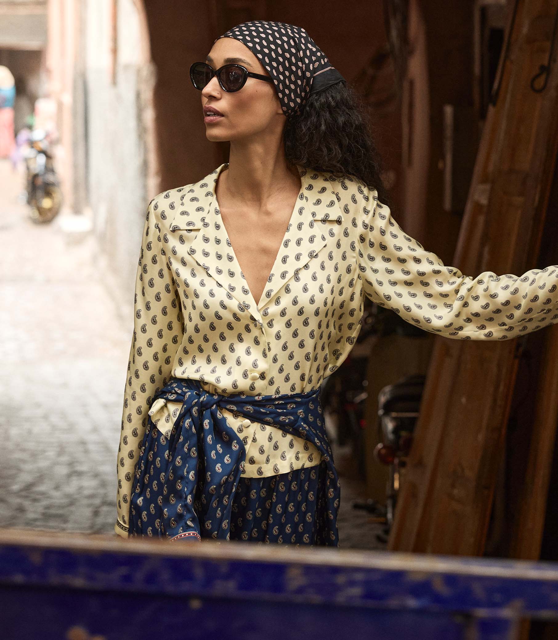 Woman wearing a yellow patterned blouse and headscarf in an urban setting