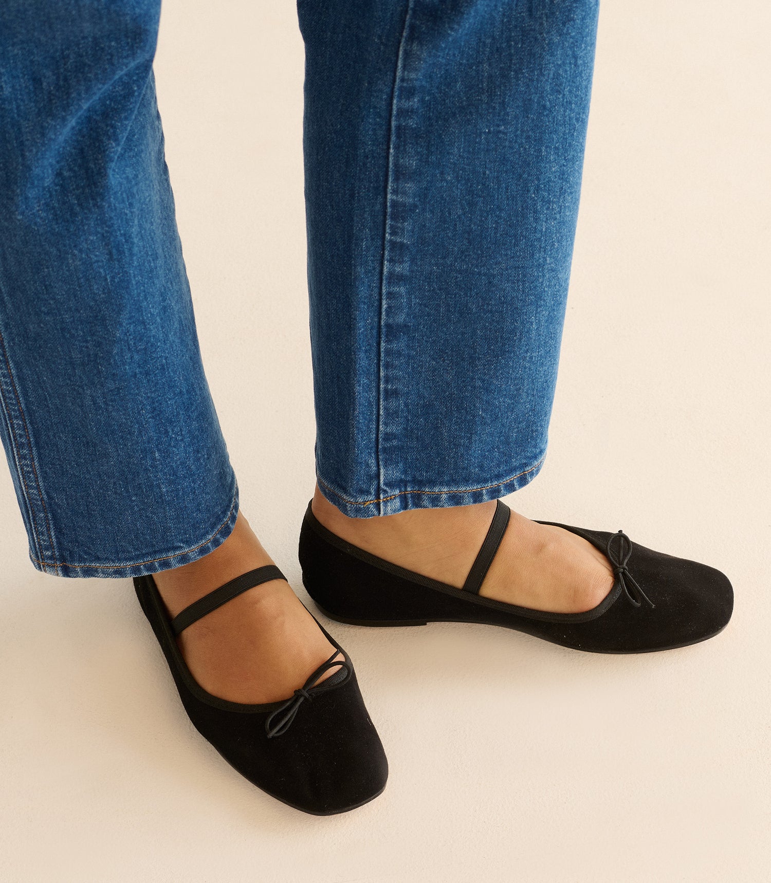 Black flats worn with blue jeans on a light background