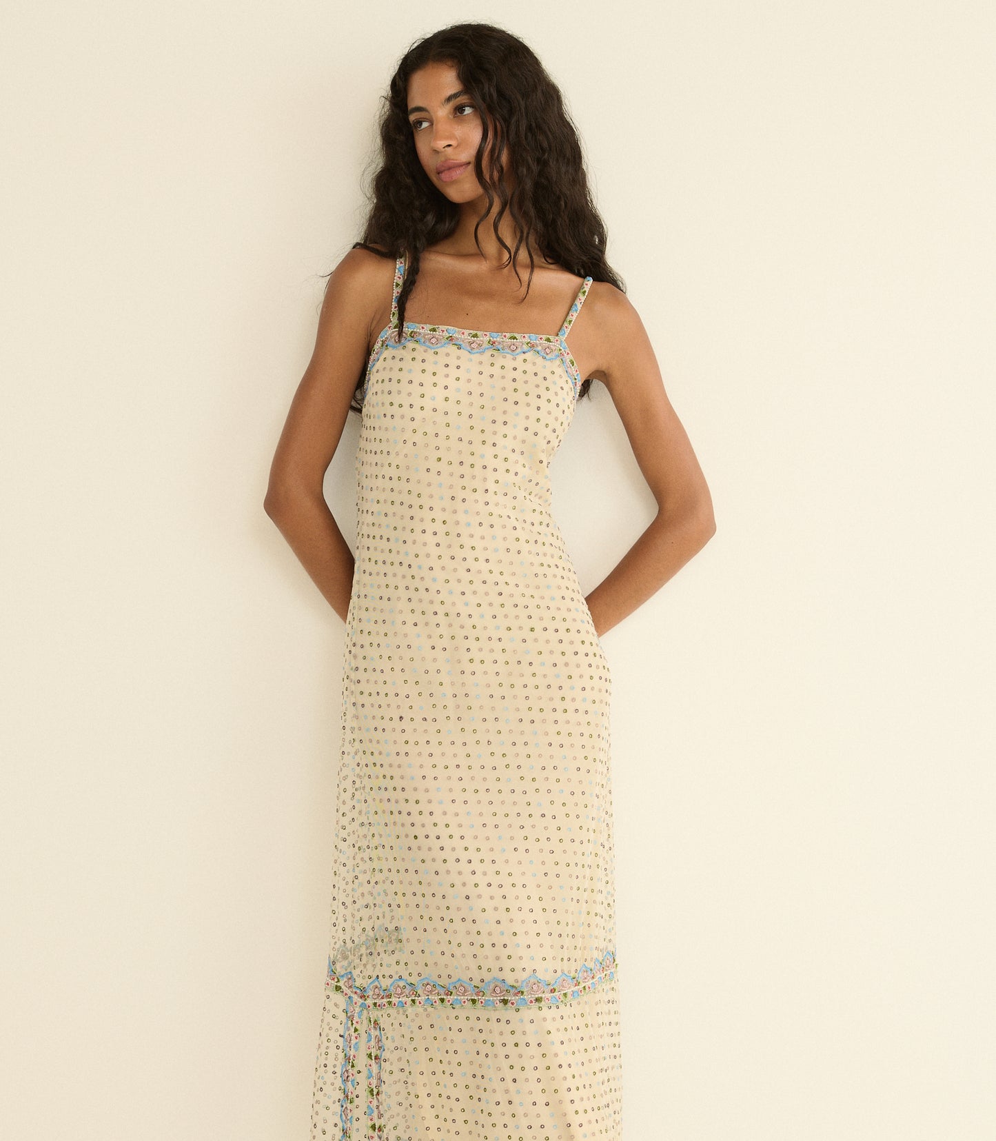 Woman wearing a beige patterned dress with blue trim against a plain background